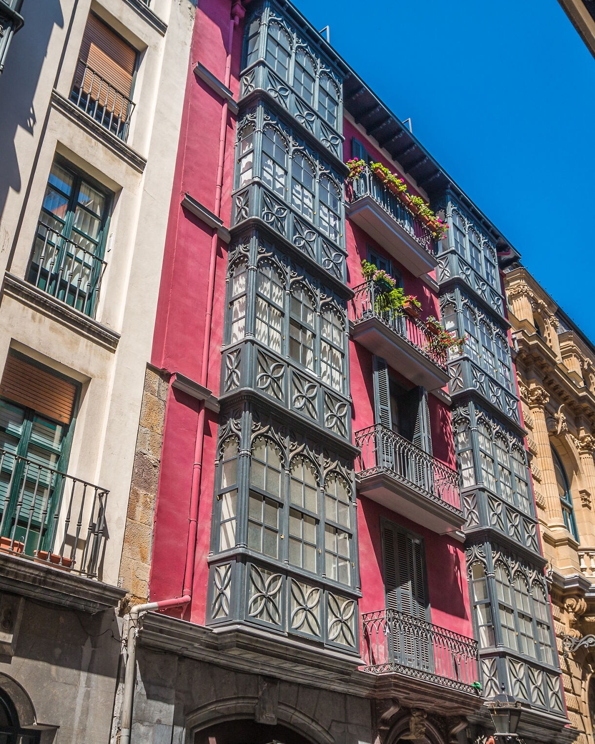 Close-up view of historic buildings in Bilbao’s Old Town, featuring colorful walls and decorative wrought-iron balconies under a bright blue sky.