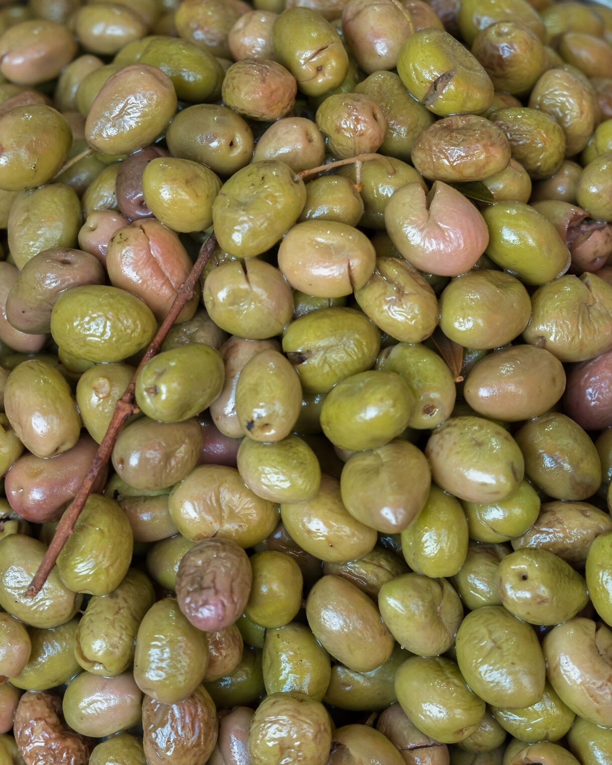 Close-up of glossy green olives piled together in a large container.