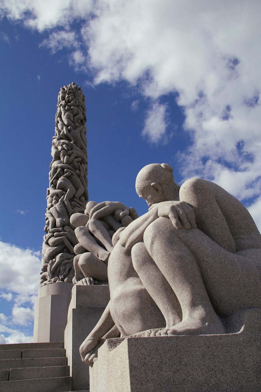 Vigeland Sculpture Park's iconic Monolith in Oslo, Norway, featuring intricately carved human figures intertwined in a towering granite column under a bright, cloudy sky.