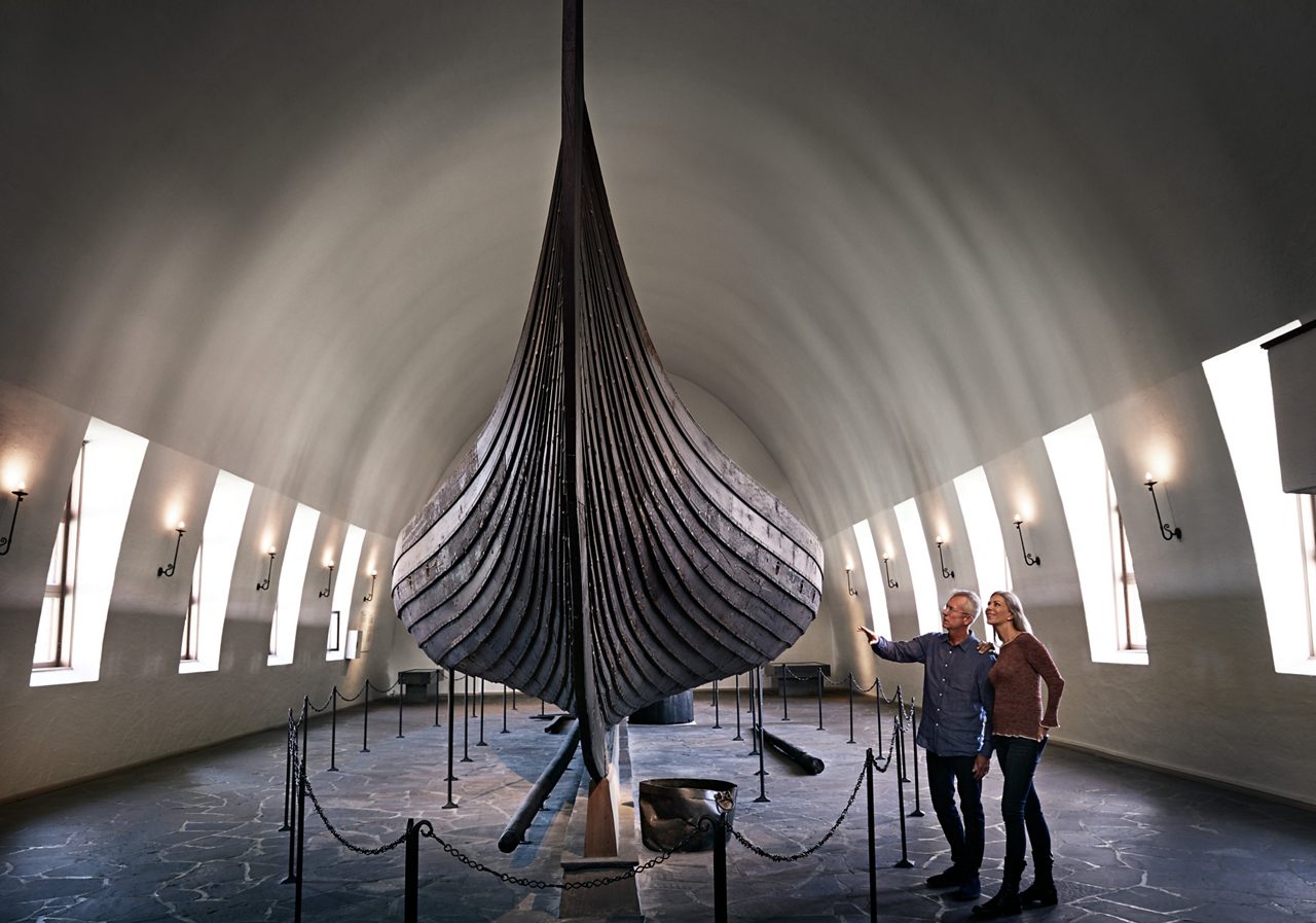 Museum exhibit featuring a large Viking ship, a man gesturing in awe.