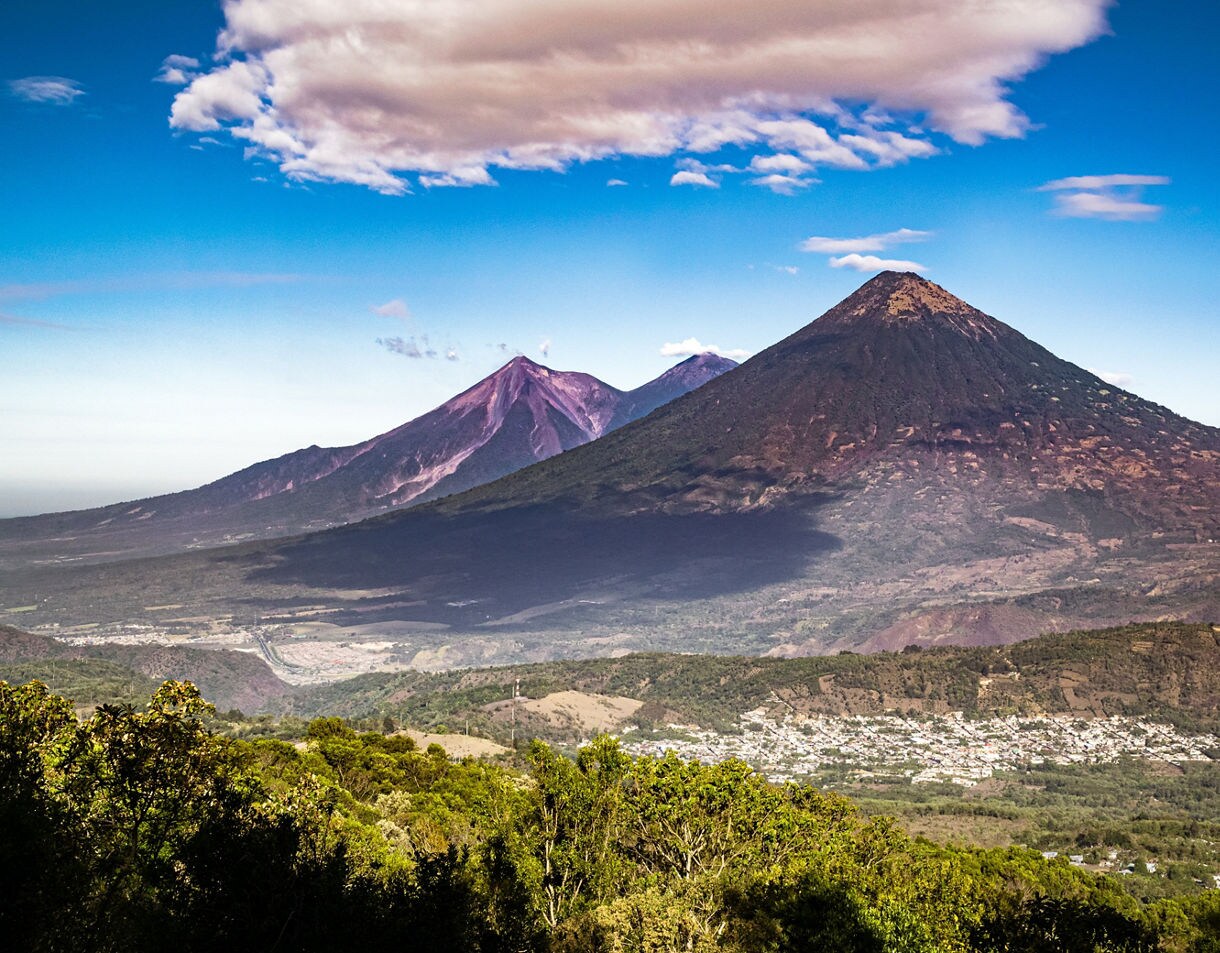 Expansive view of Guatemala’s volcanic landscape showing Volcán de Agua in the foreground and Volcán de Fuego and Acatenango in the distance under a clear blue sky.