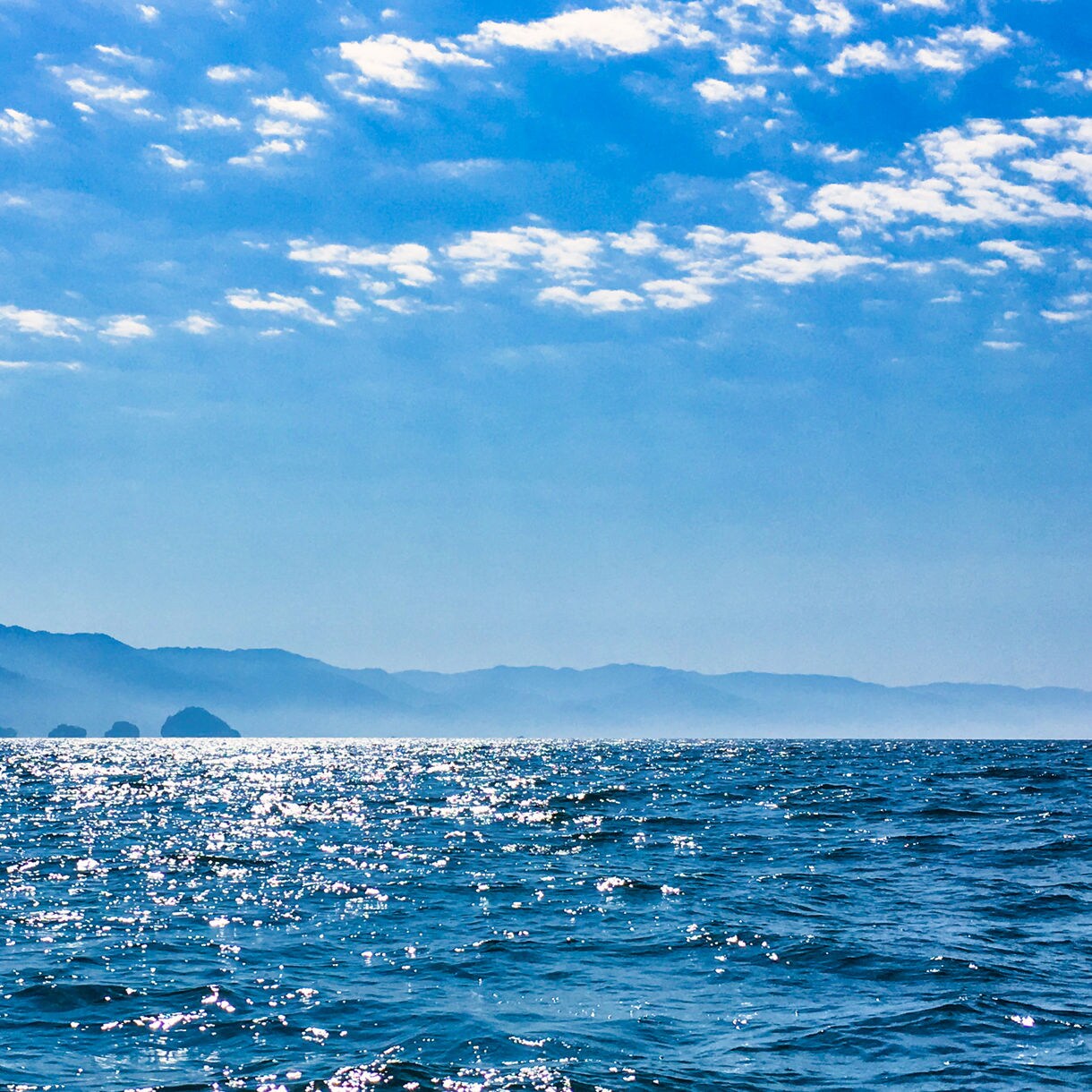 Sparkling ocean waters with distant mist-covered mountains near Puerto Vallarta under a partly cloudy sky.