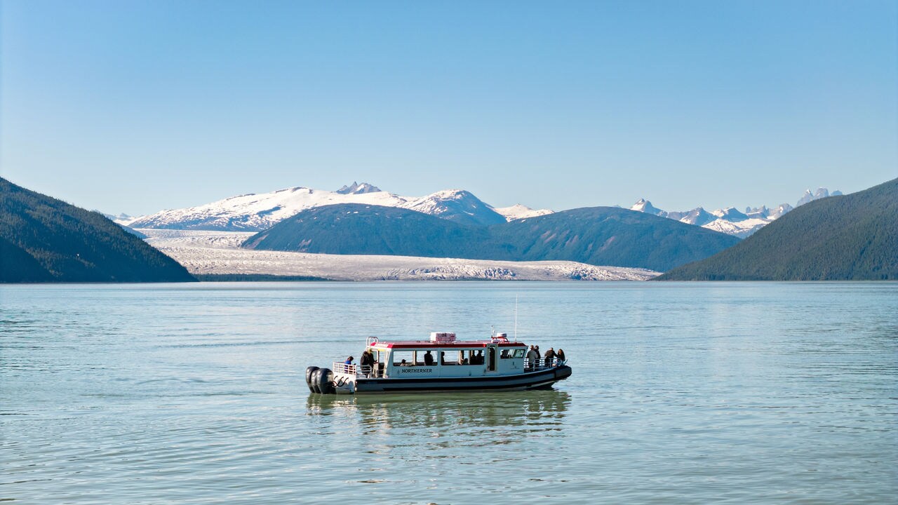 A small tour boat floats on a calm, expansive lake surrounded by mountains. 