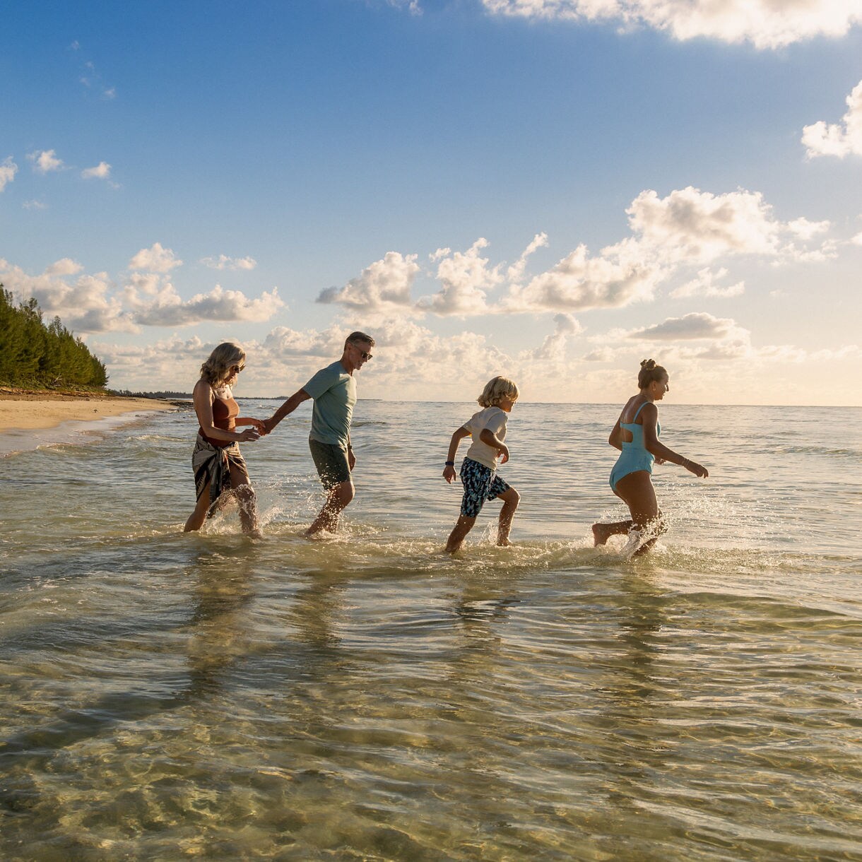 Family of four playing in shallow turquoise waters on a Caribbean beach at golden hour, with lush coastline in the background.