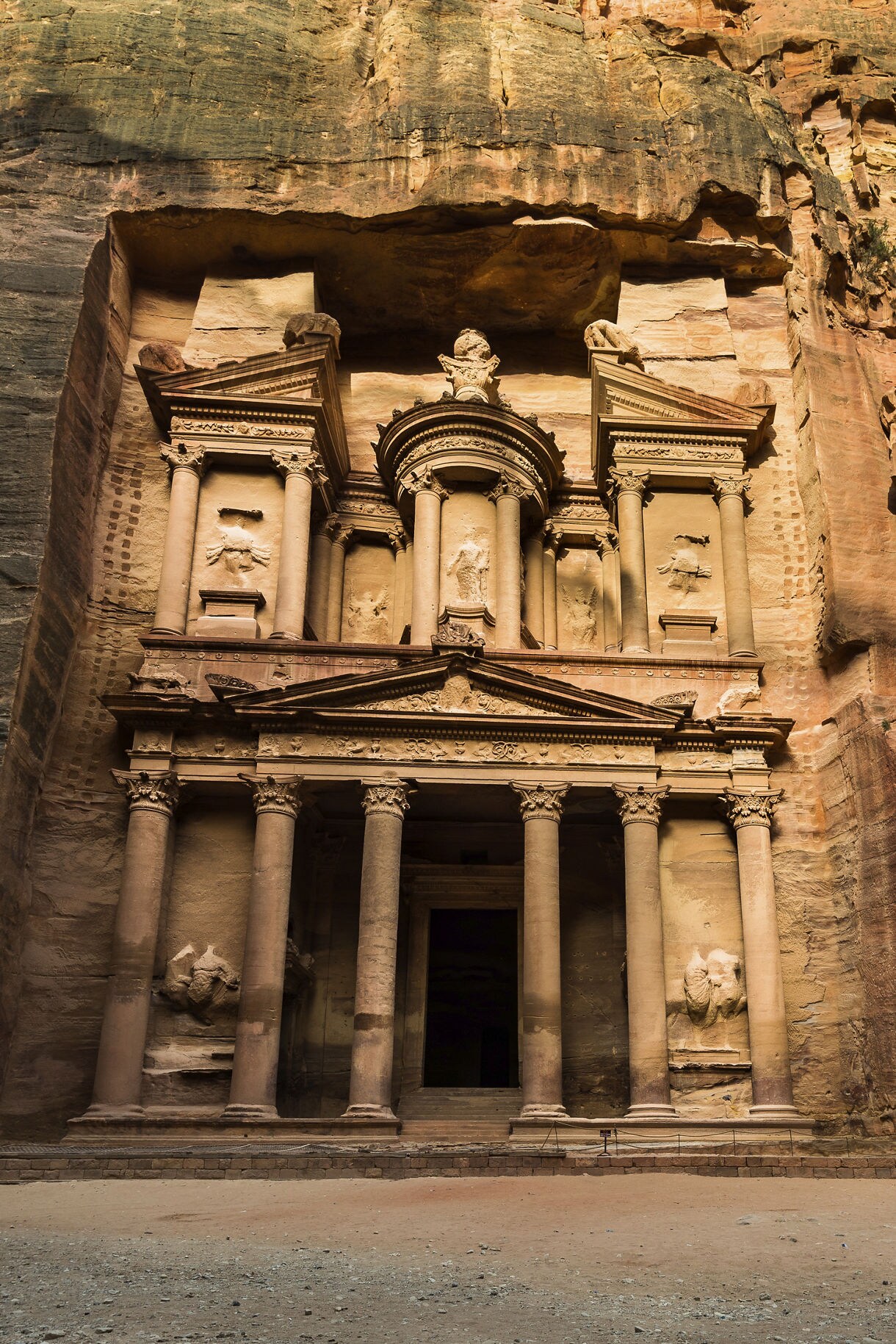 View of the ancient city of Petra in Jordan, featuring the iconic rock-cut architecture of the Treasury, with its intricate facade carved into the rose-red sandstone cliffs.