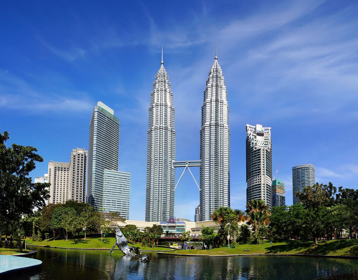 he Petronas Twin Towers in Kuala Lumpur rising above the skyline with a park and reflective pond in the foreground.