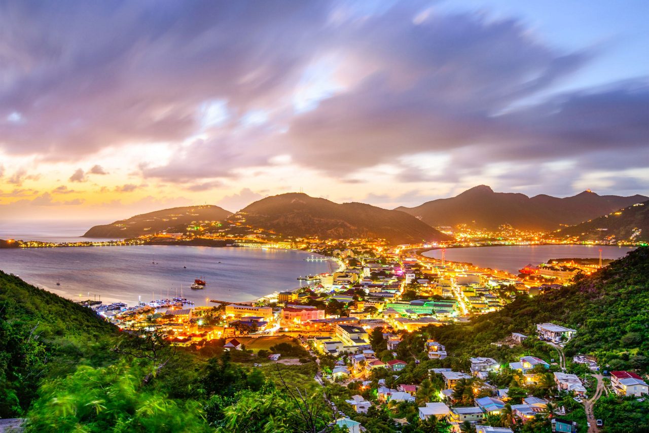 Panoramic twilight view of Philipsburg town illuminated with golden lights nestled between mountainous coastline and calm harbor waters