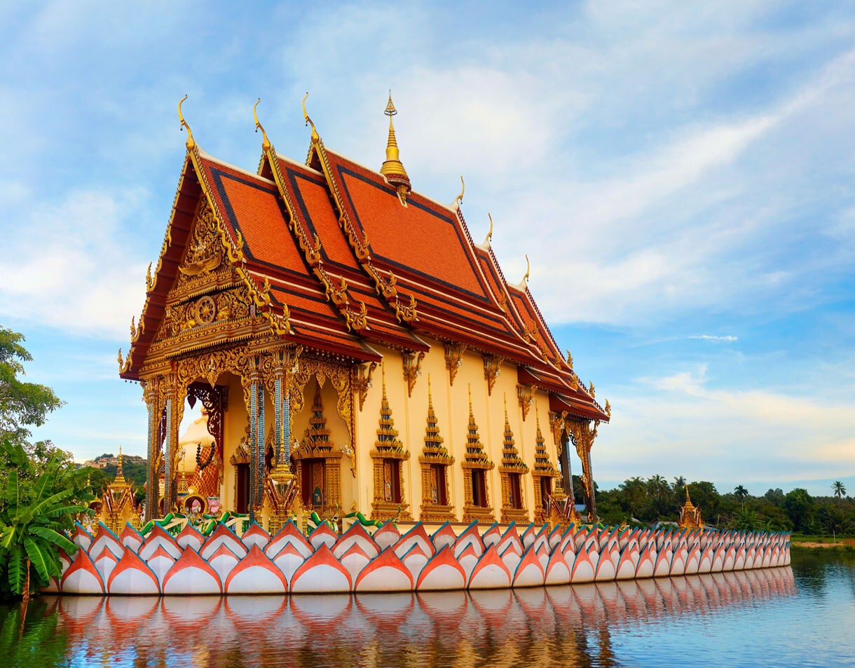 Ornate temple at Wat Plai Laem in Koh Samui with golden carvings, red roof tiles and a reflection shimmering in the surrounding pond.