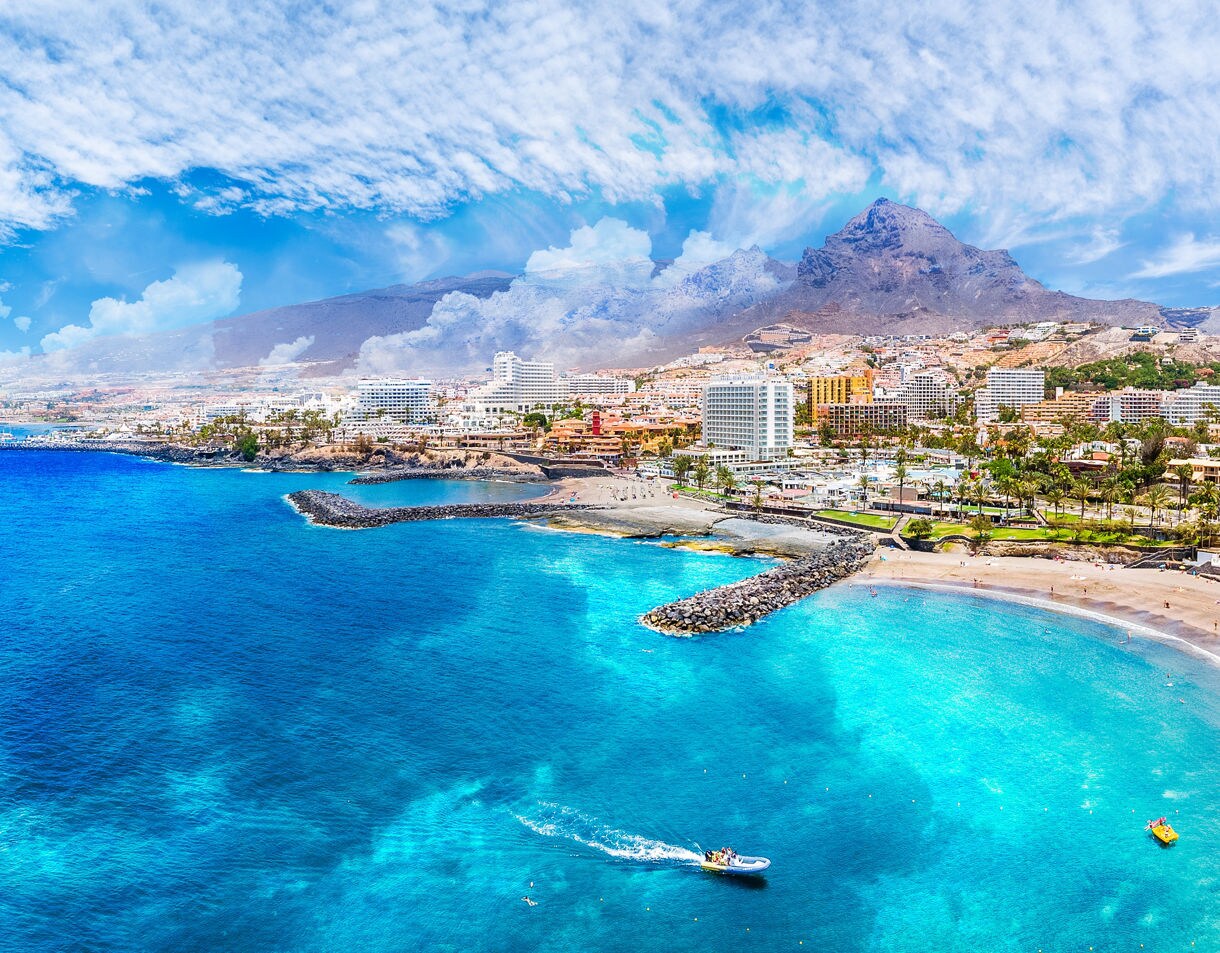 Aerial view of Playa de las Américas in Tenerife with turquoise water, sandy beaches and a bustling resort town backed by mountains.