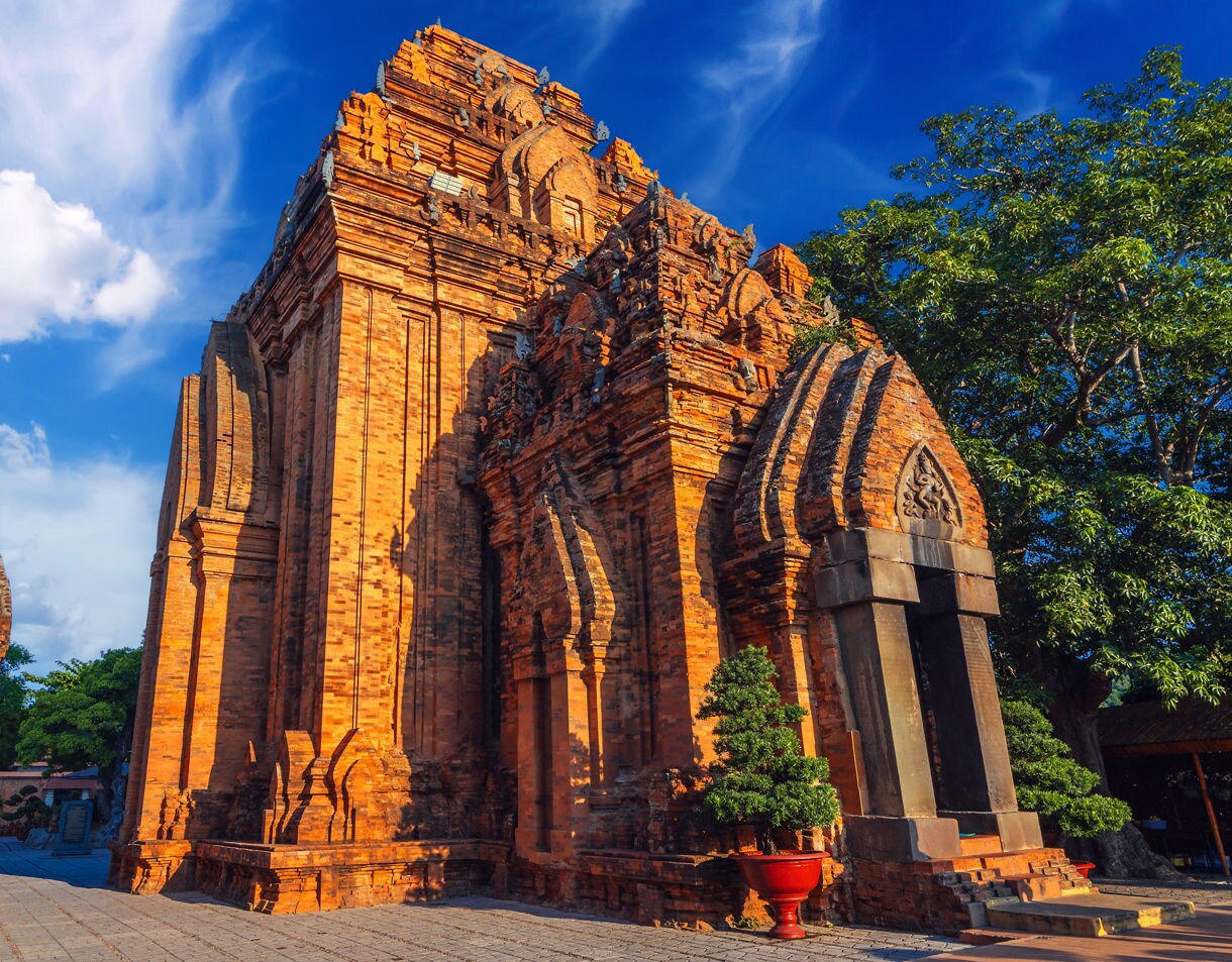 The Po Nagar Cham Tower in Nha Trang, Vietnam, bathed in warm sunlight with vivid orange brickwork and a deep blue sky above.