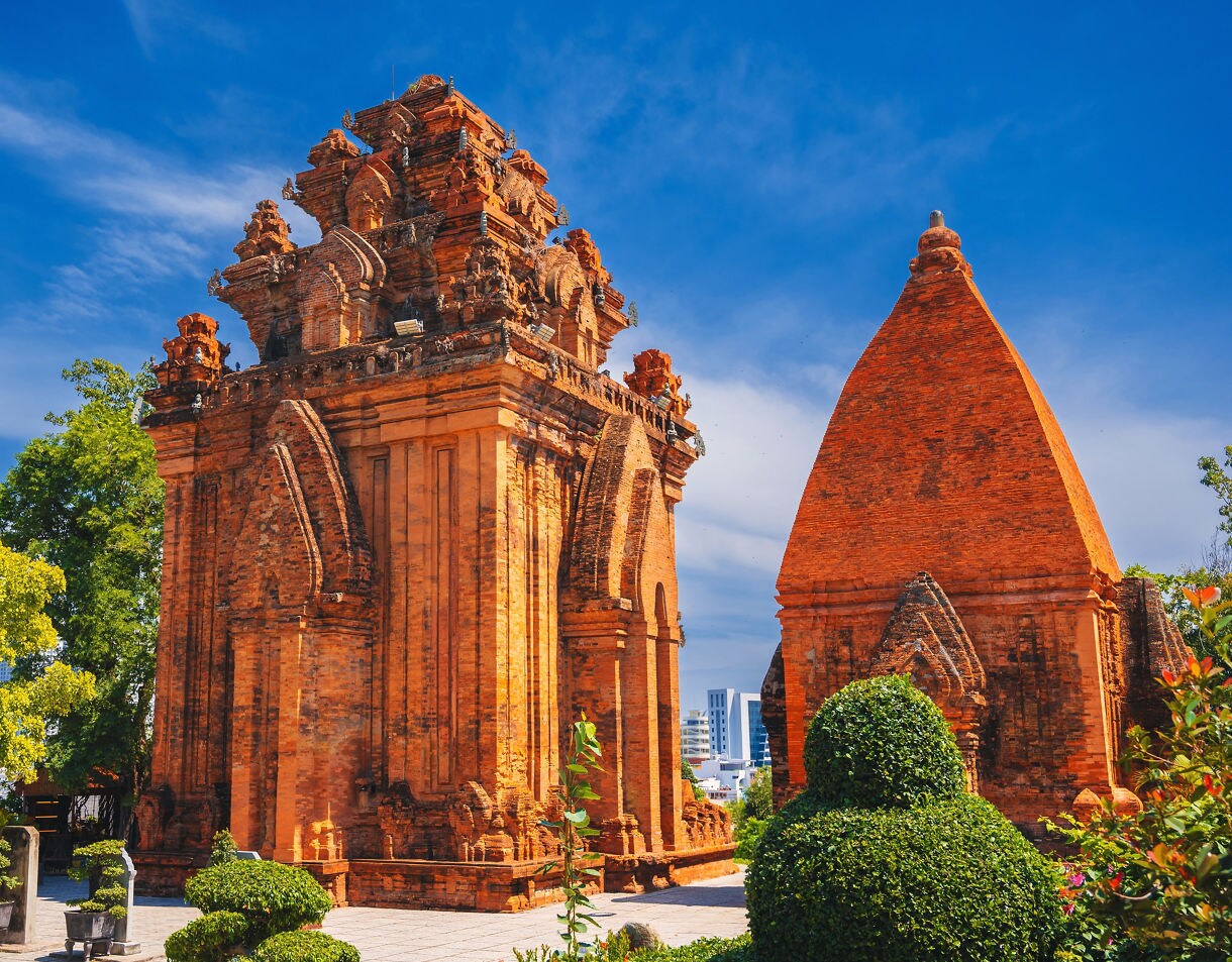The red-brick Po Nagar Cham Towers in Nha Trang, Vietnam, surrounded by manicured greenery under a bright blue sky.