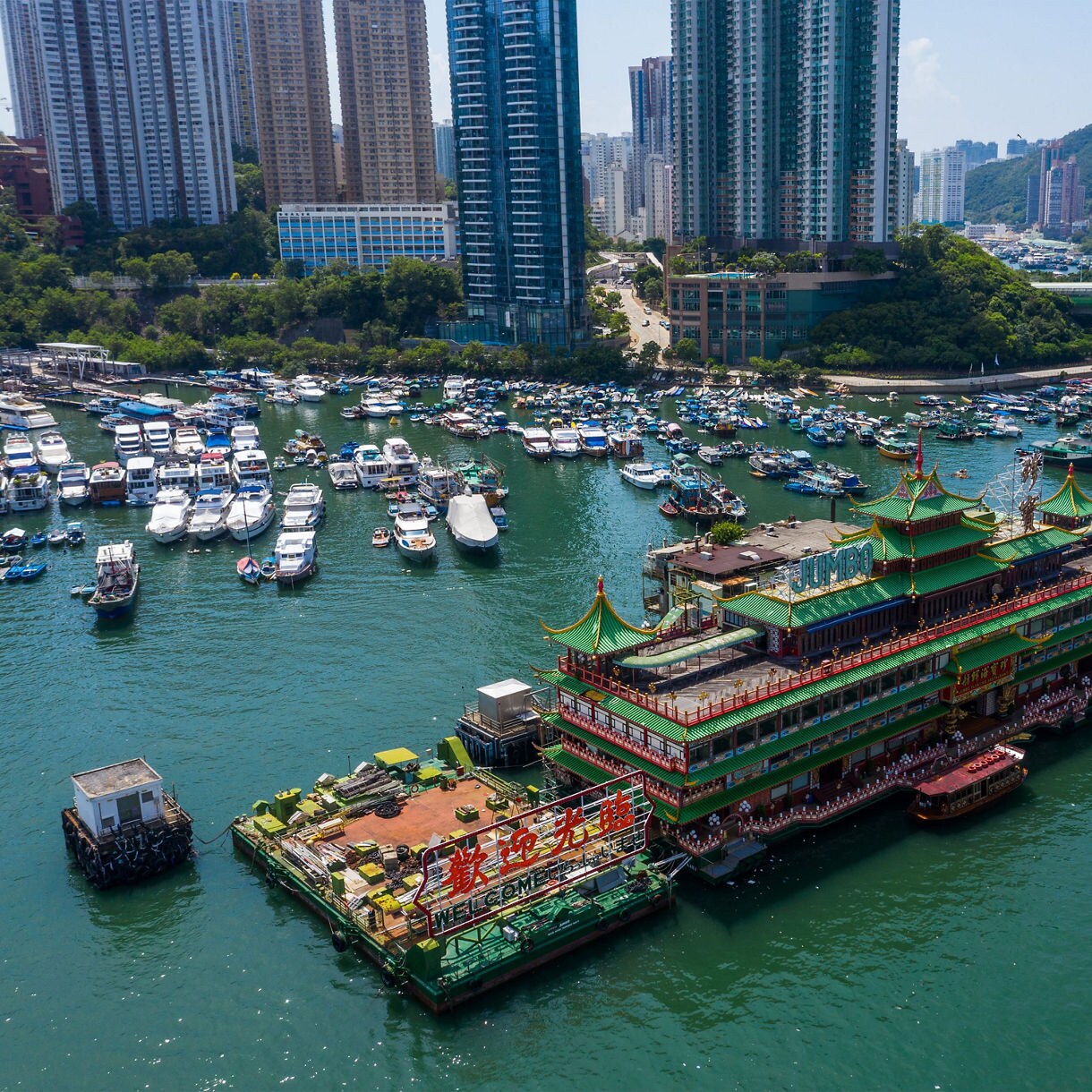 Aerial view of Aberdeen Harbour in Hong Kong featuring the ornate floating restaurant and moored boats surrounded by high-rise buildings.