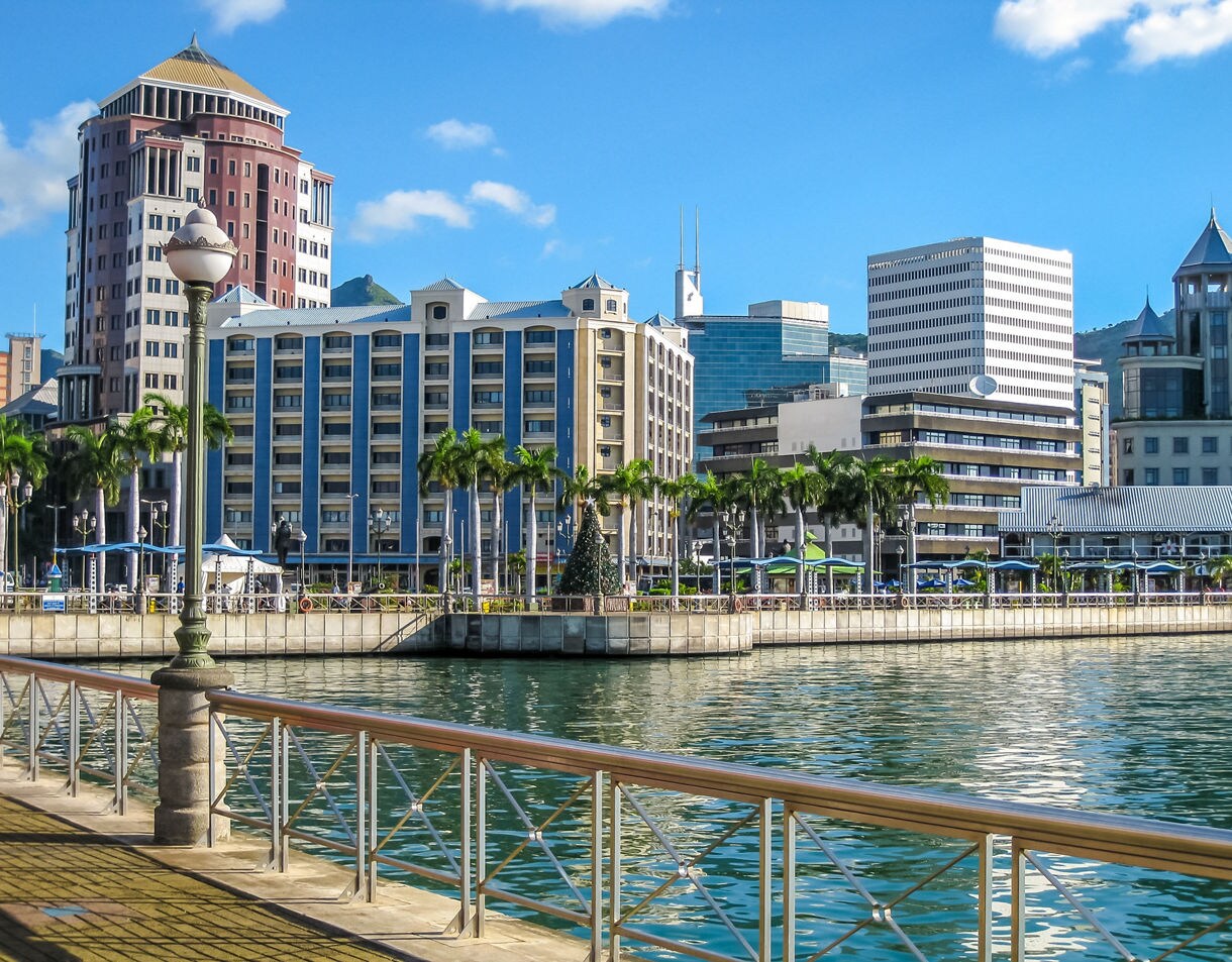 Port Louis waterfront in Mauritius with modern high-rise buildings, palm trees and calm turquoise water on a sunny day.