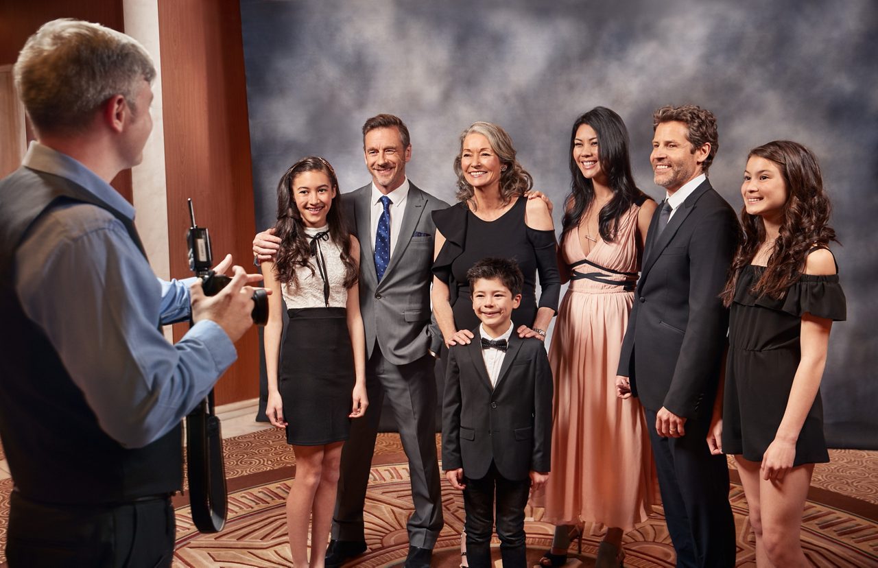 A photographer with a camera on a tripod takes a formal portrait of a multigenerational family dressed up for a special occasion.