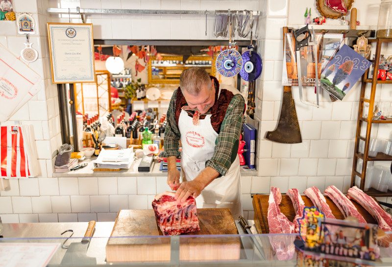 A butcher working at a counter preparing cuts of meat in a traditional butcher shop setting.