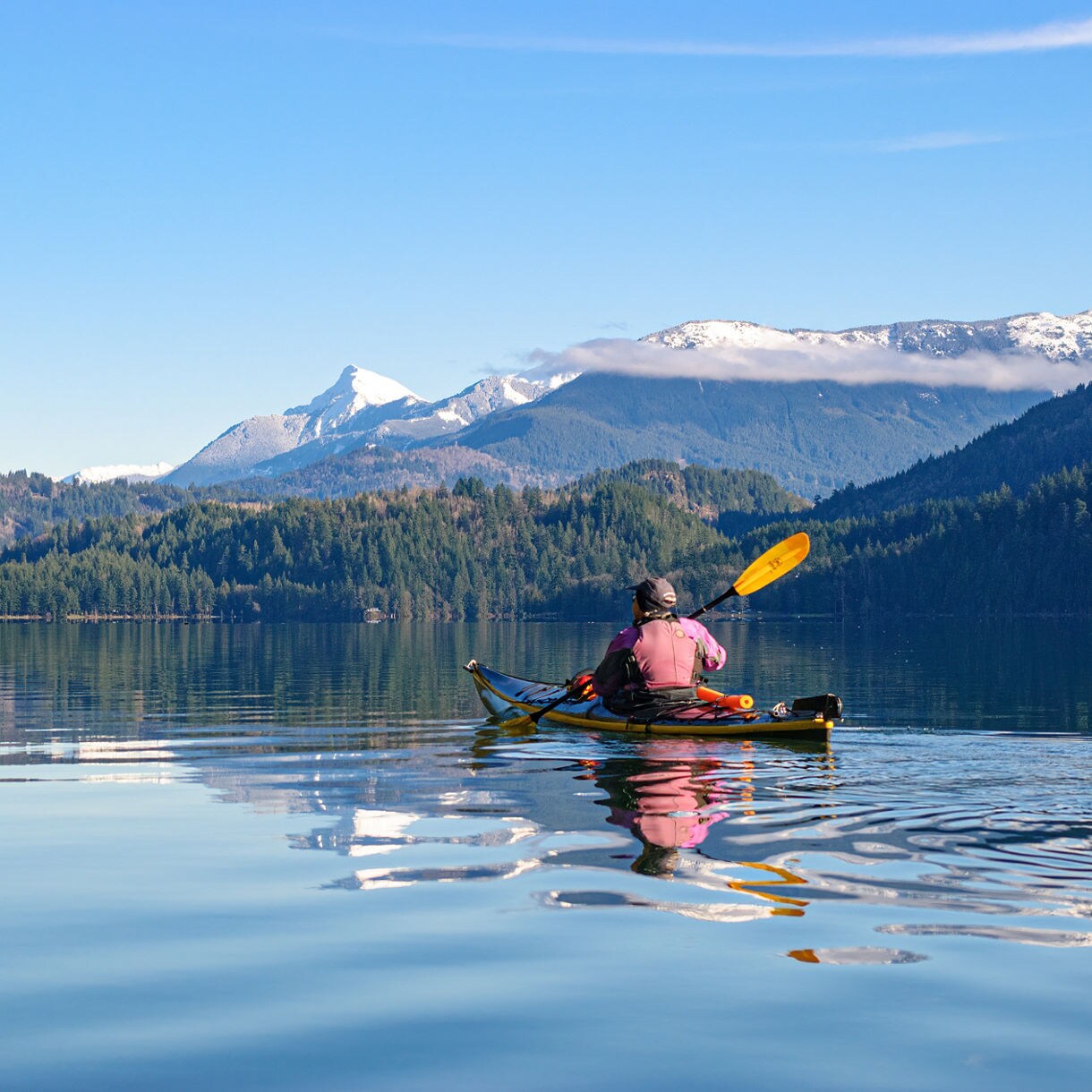Person kayaking on a calm lake near Prince Rupert, British Columbia, with reflections on the water, forested shoreline.