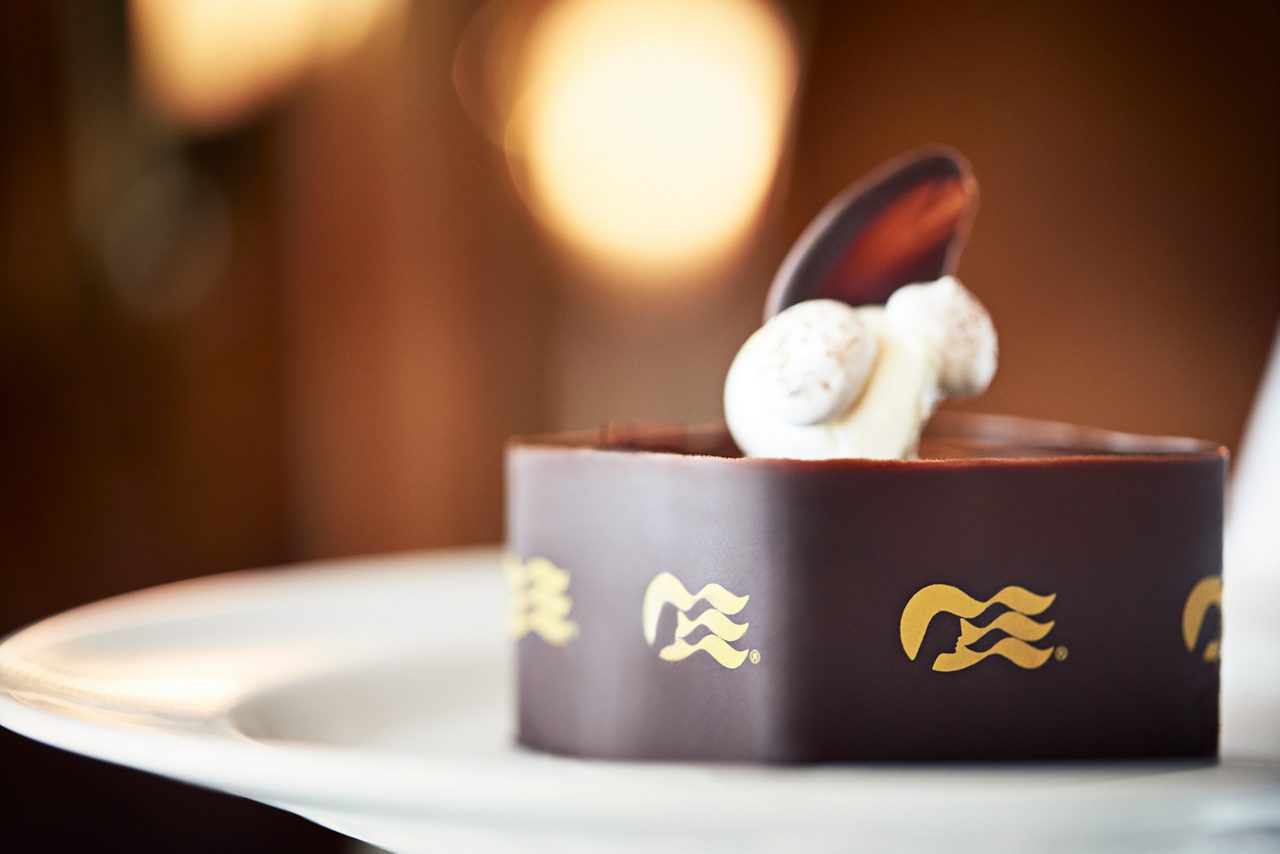 A close-up of a decadent chocolate dessert topped with cream, garnished with the Princess Cruises logo.