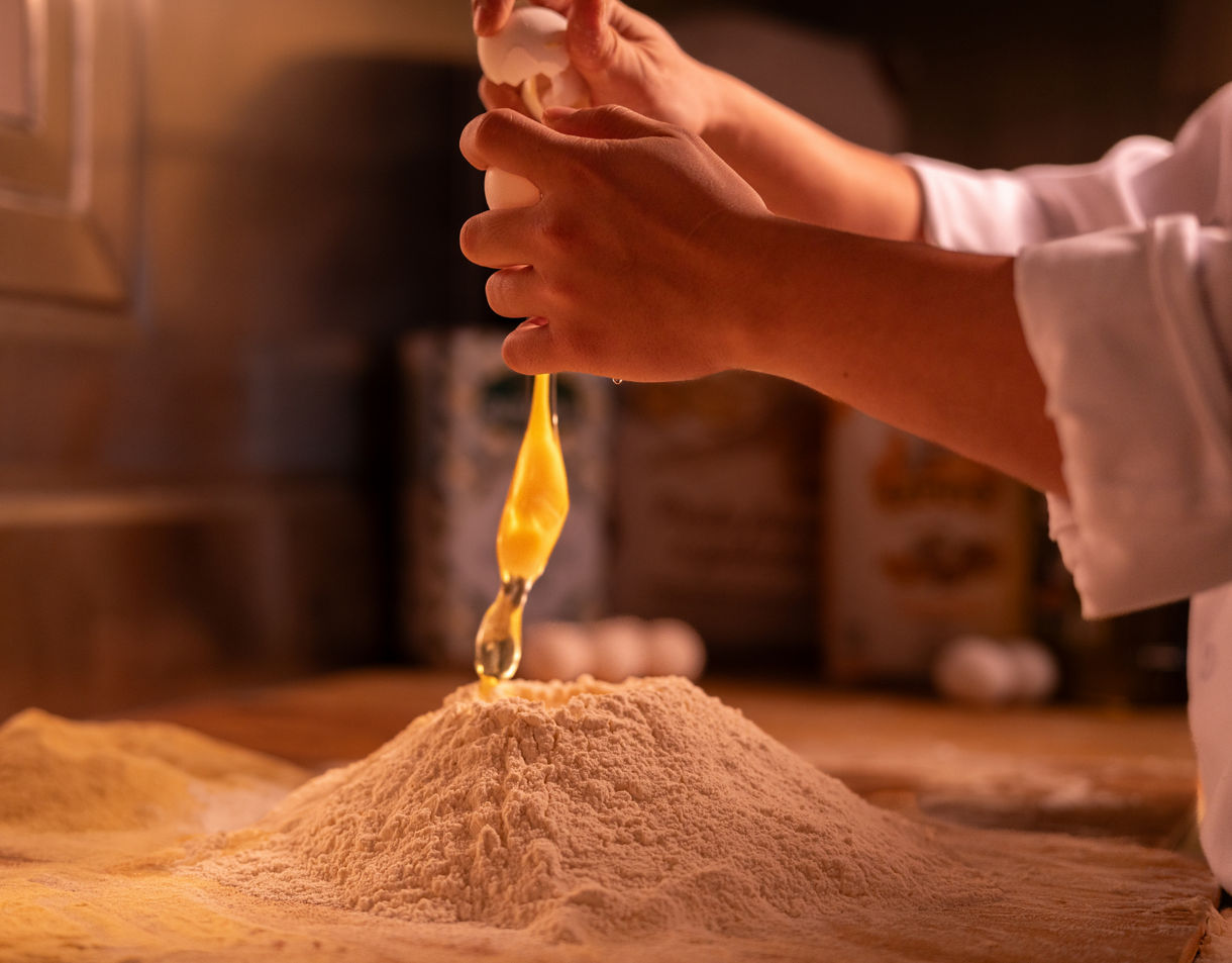 Chef Cracking Egg Into Flour On Kitchen Counter