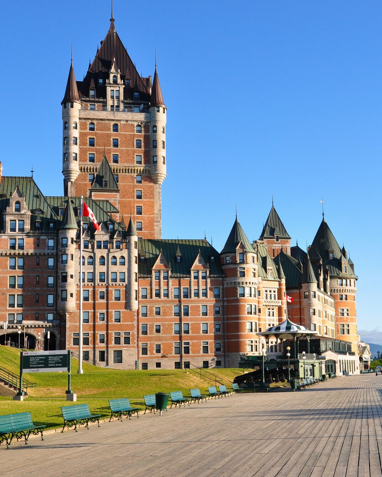 Château Frontenac beside Dufferin Terrace boardwalk under a clear blue sky.