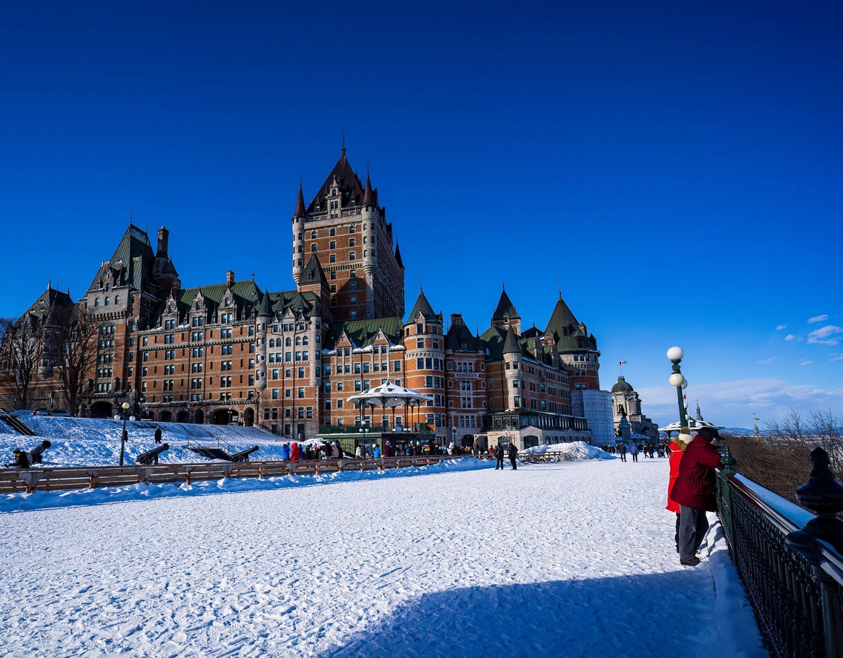 Snow-covered Dufferin Terrace with people strolling near Château Frontenac on a clear winter day.