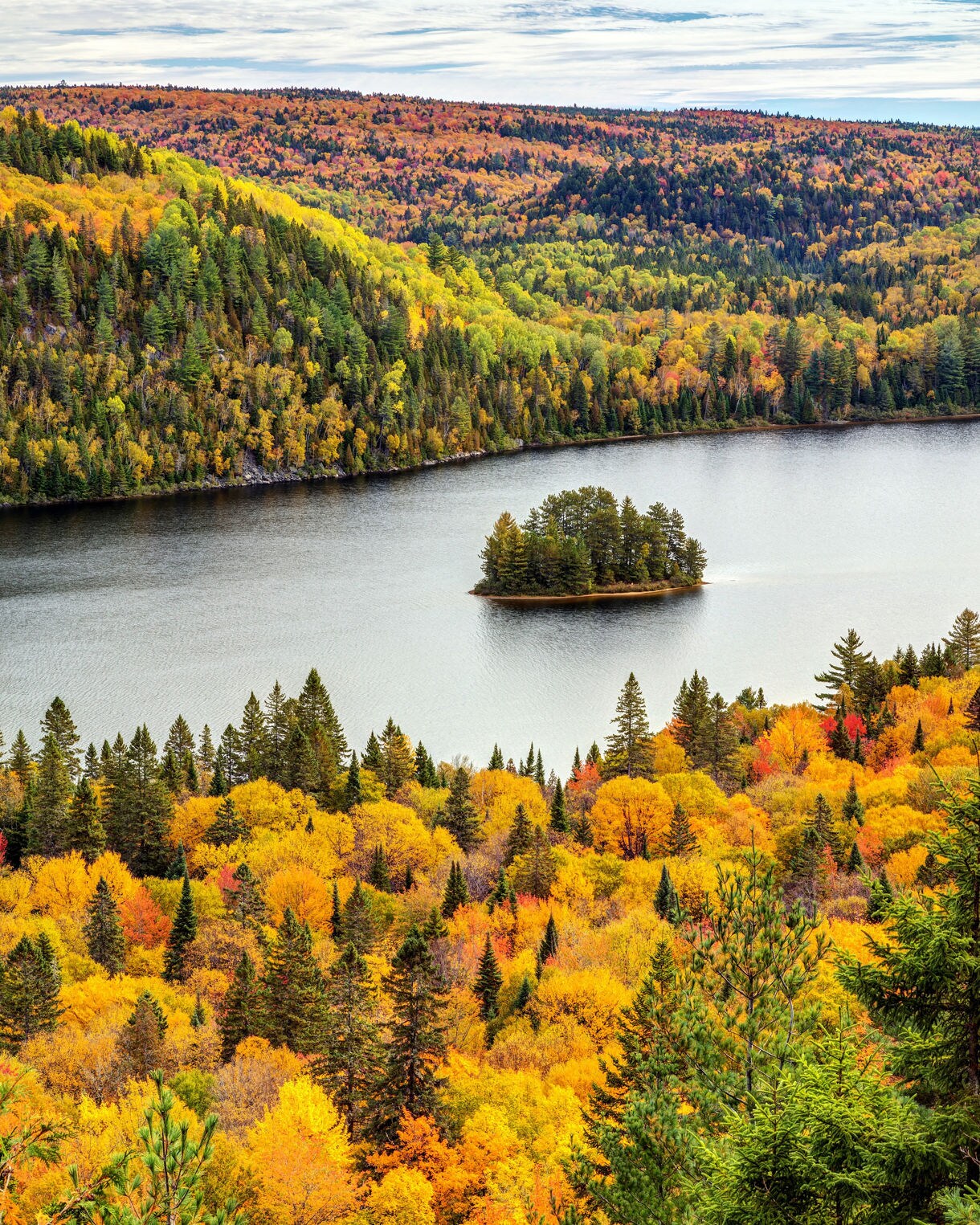 Lake with small island surrounded by rolling hills covered in vivid fall foliage.