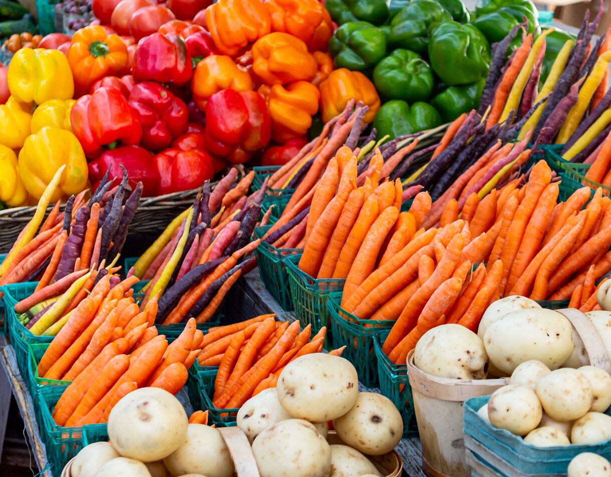 Baskets of multicolored carrots, bell peppers and potatoes displayed at a farmers market.