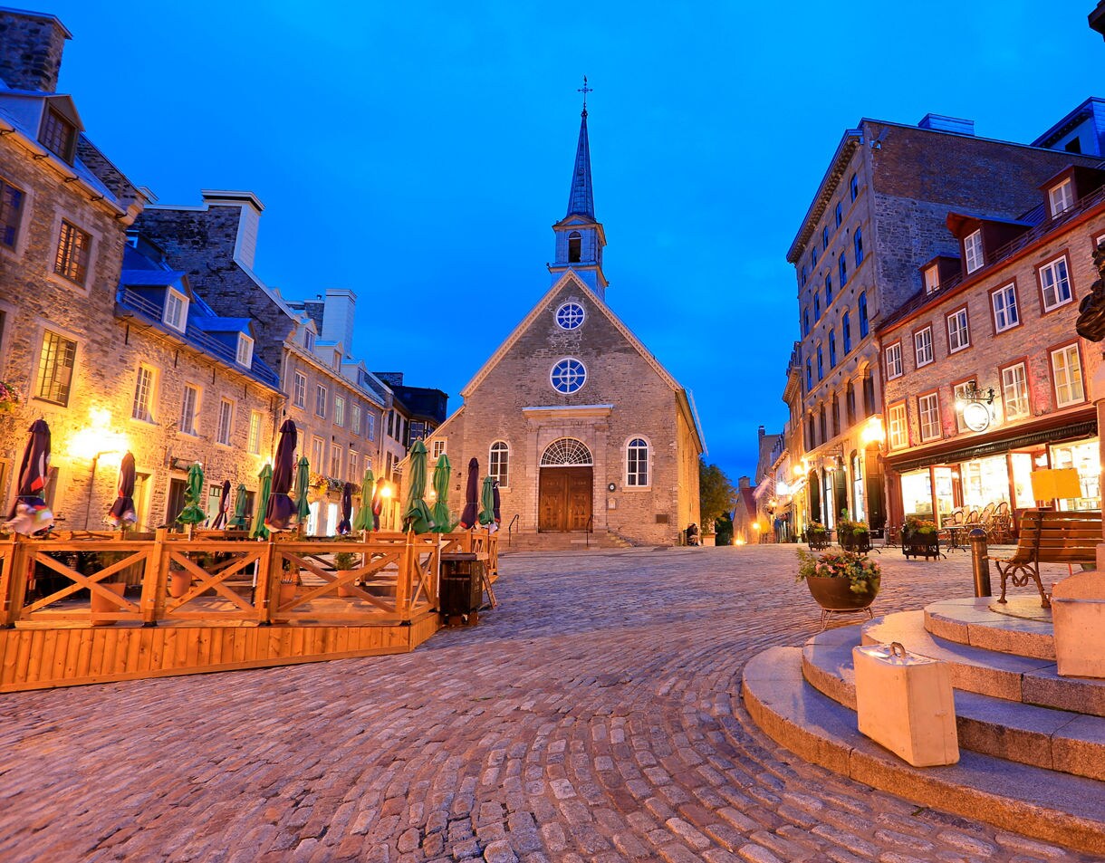 Evening view of Place Royale in Old Québec with stone church and cobblestone square lit by warm lights.