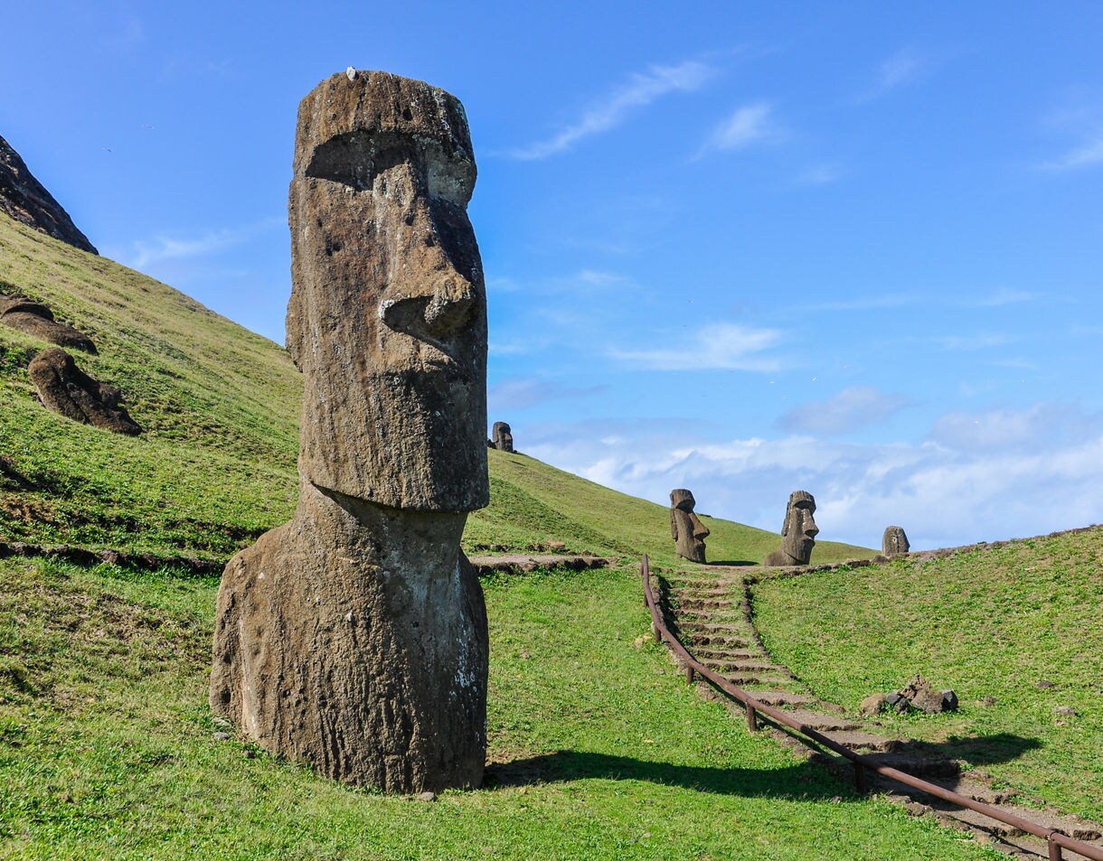 Partially buried moai statues standing along the green hills of Rano Raraku on Easter Island under a bright blue sky.