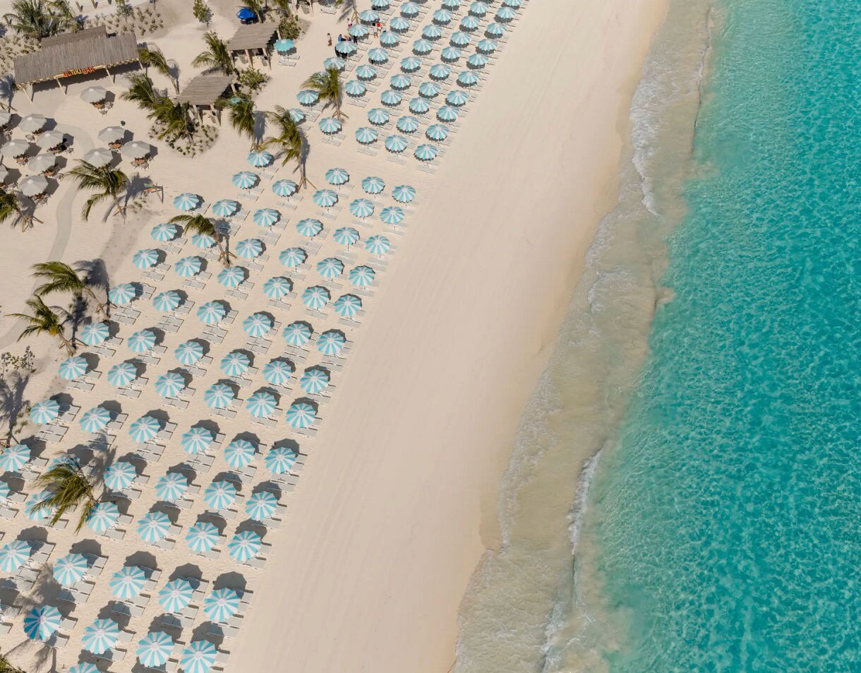 This image captures a sweeping aerial perspective of a curved white sand beach meeting vibrant turquoise waters
