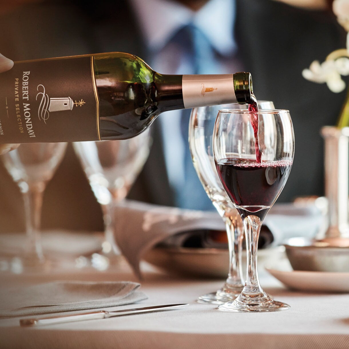 Five cups on the table, one is being filled with red wine