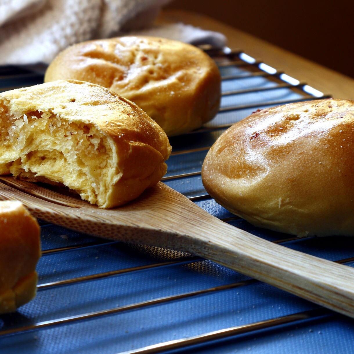 Golden brown bread rolls cooling on wooden cutting board with kitchen utensils in background