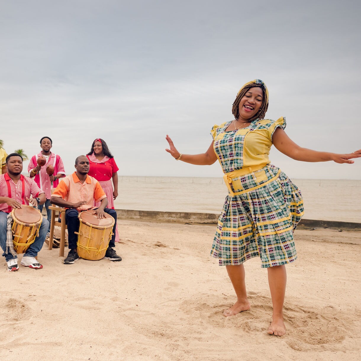 A Garifuna dance group performing on a sandy beach in Roatán, with colorful traditional outfits and lively drumming, as a dancer leads the celebration with graceful movements.
