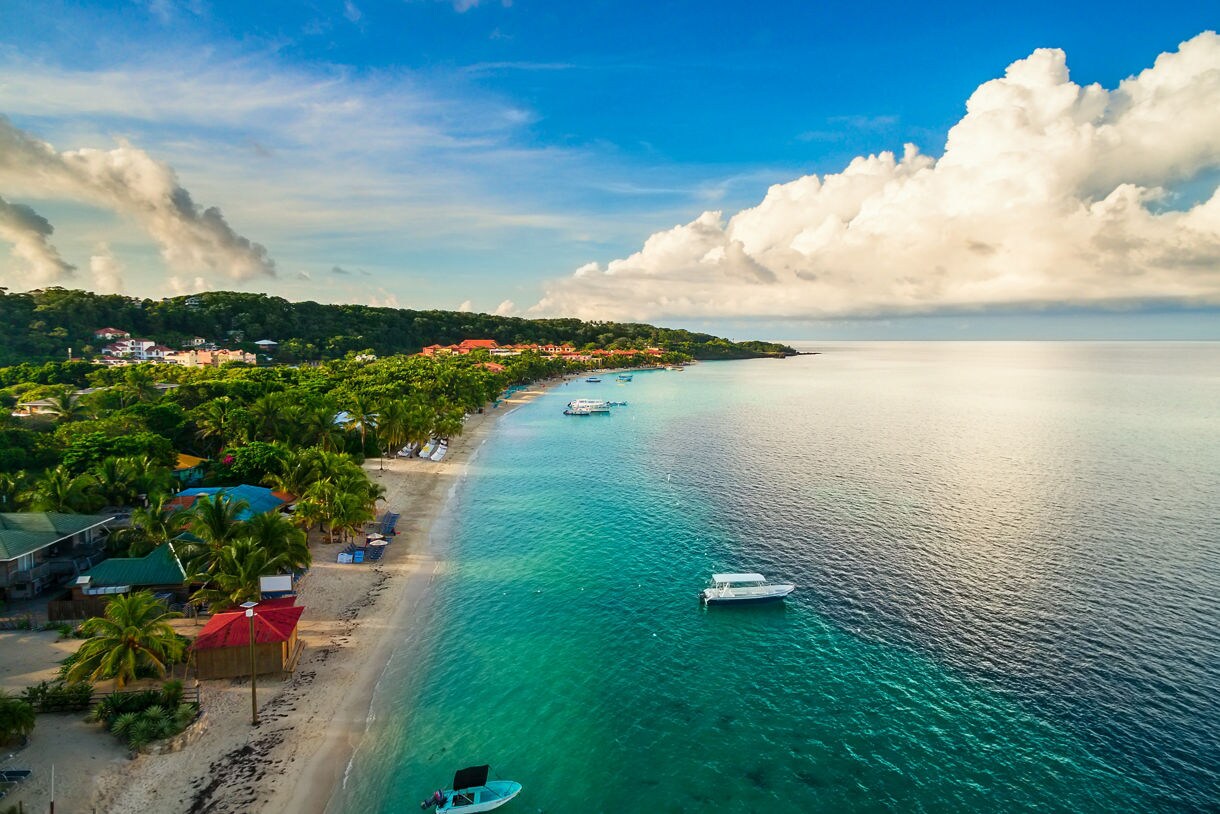 Roátan shoreline with anchored boats in water.