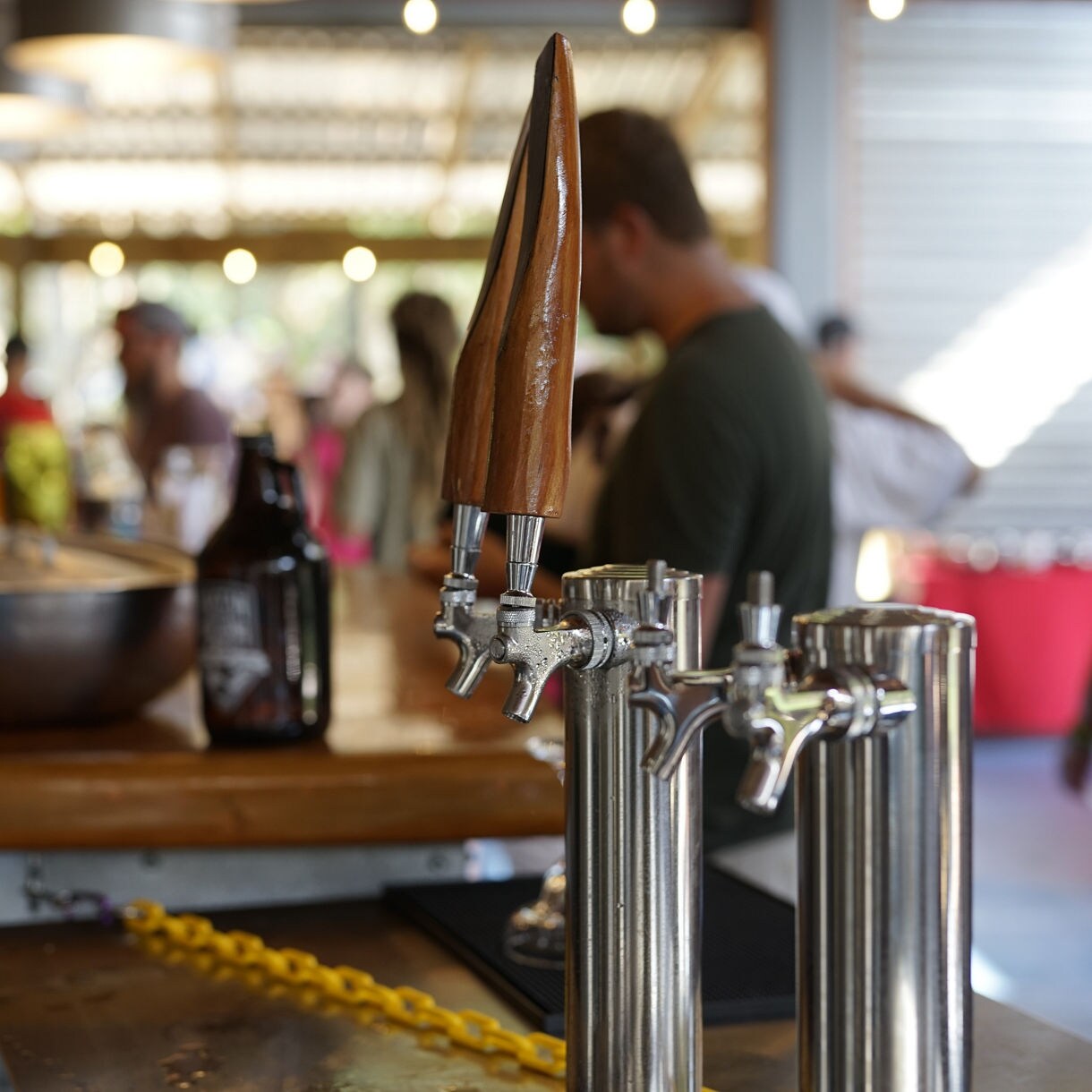 Wooden beer tap handles at bar counter with bartender working in blurred background under warm lighting