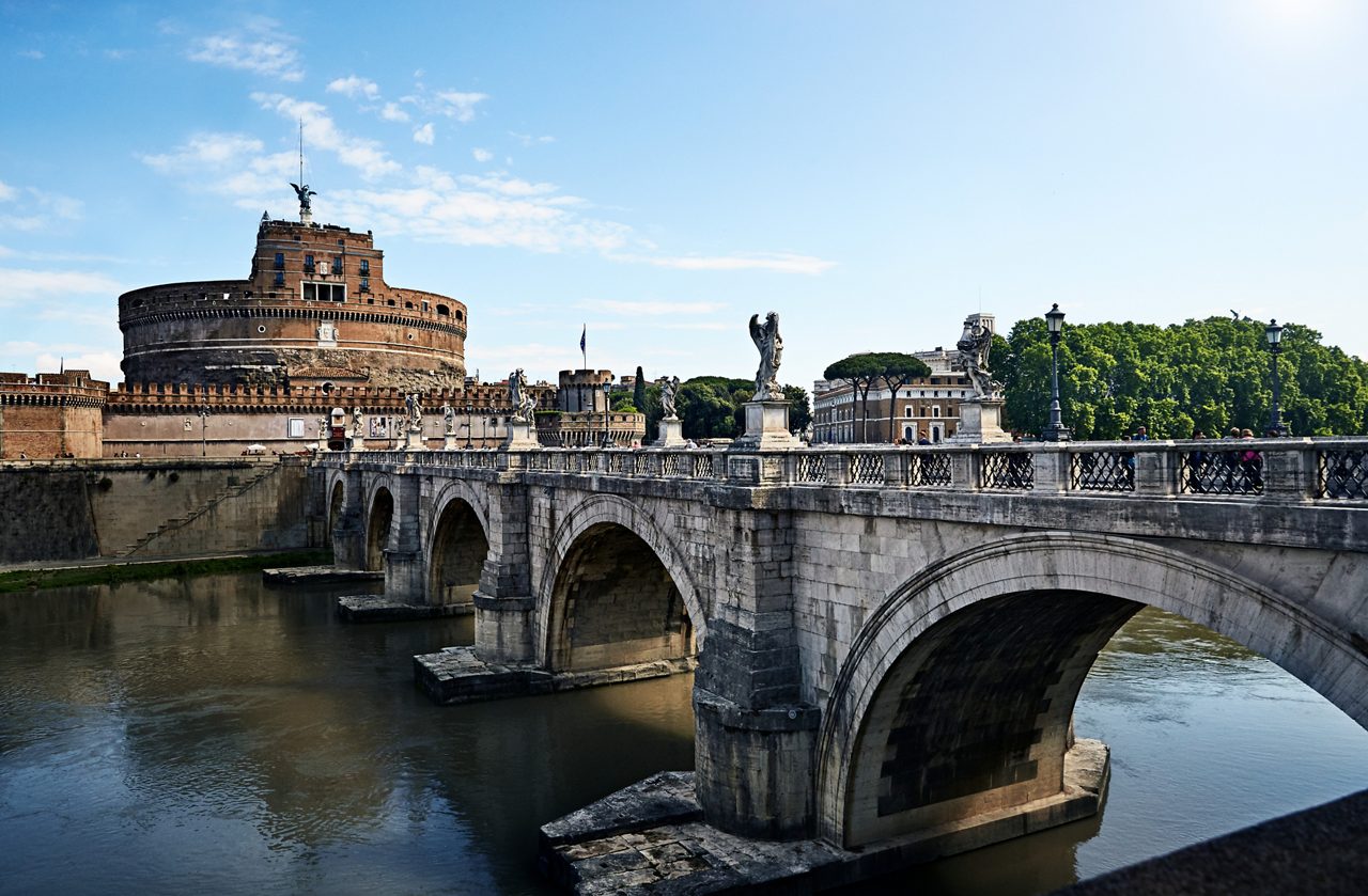 The Castel Sant'Angelo and the Bridge of Angels in Rome, Italy, with statues lining the bridge and the ancient fortress in the background, overlooking the calm river.