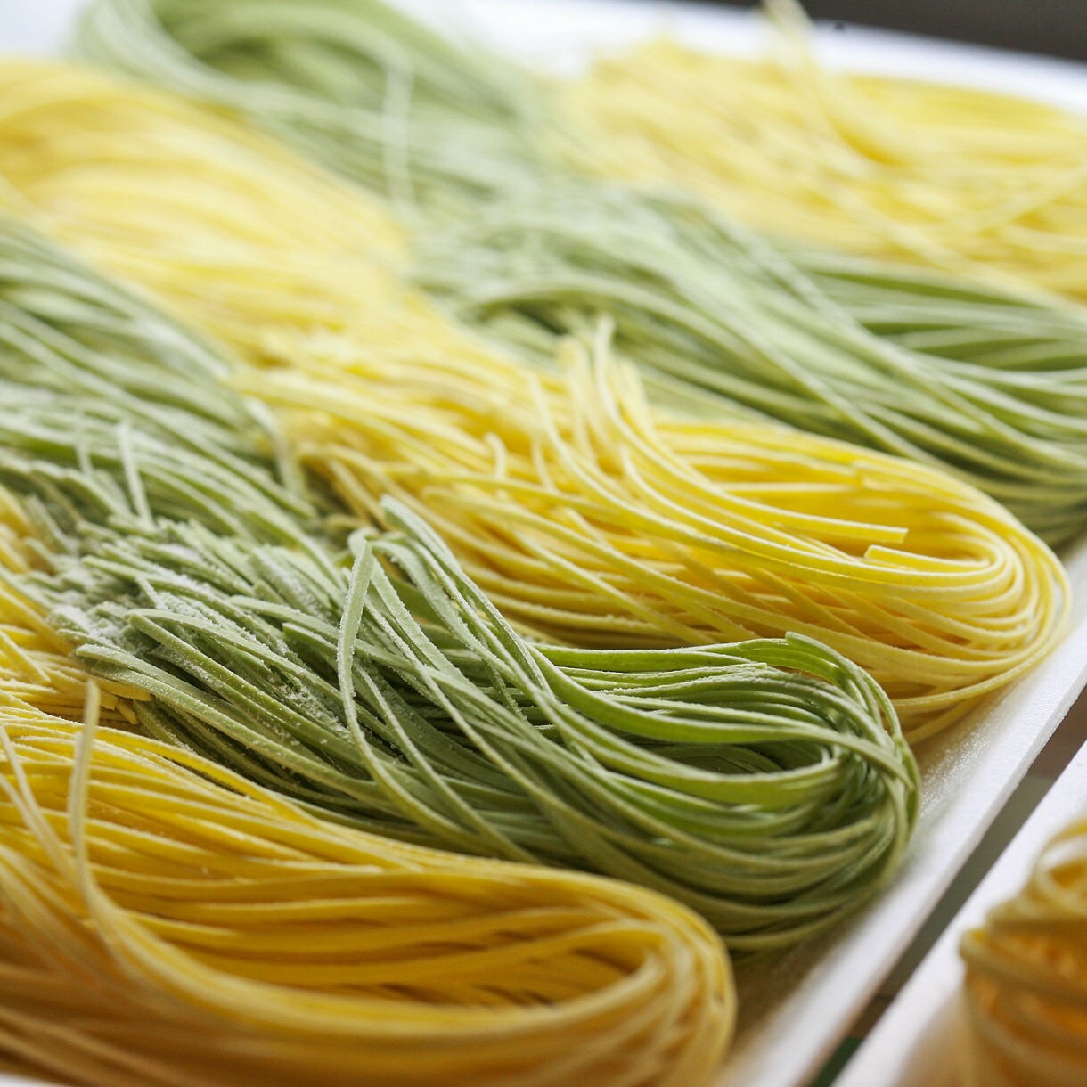 Close-up of handmade yellow and green pasta nests arranged neatly on a tray.