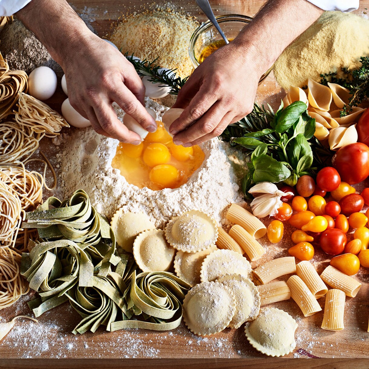 Raw, freshly made pasta strands dusted with flour arranged in loose coils on a wooden surface.