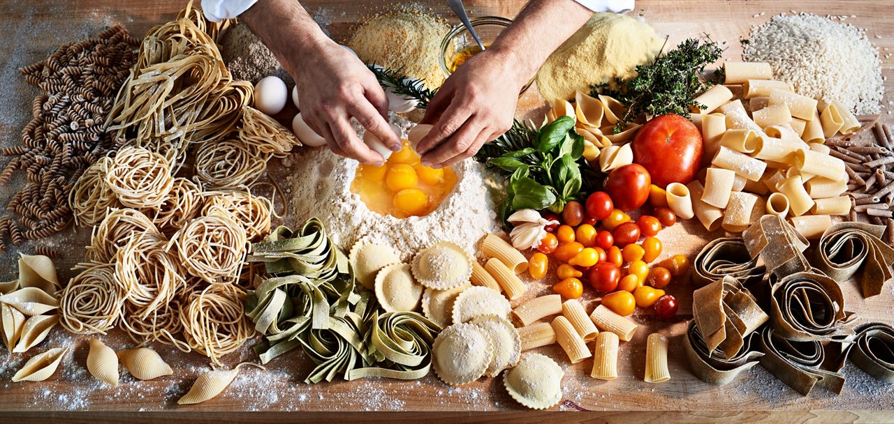 Raw, freshly made pasta strands dusted with flour arranged in loose coils on a wooden surface.