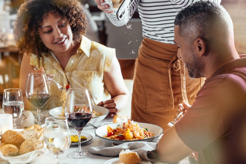 Two people enjoying an intimate meal at Sabatini's Italian Restaurant, with wine glasses, fresh bread, and plates of food on the table.