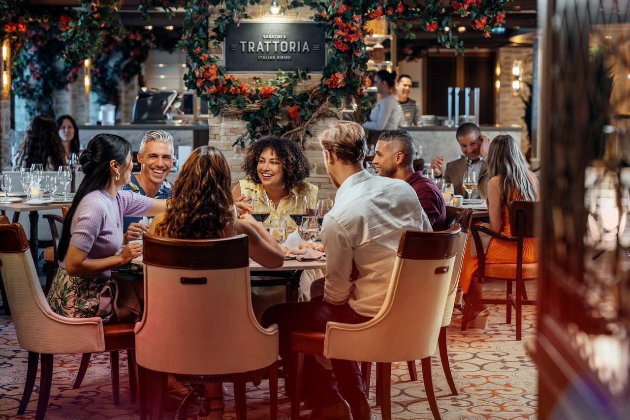 Four guests engaged in lively conversation at Sabatini's Italian Trattoria, with cocktails and wine glasses scattered across their dining table.