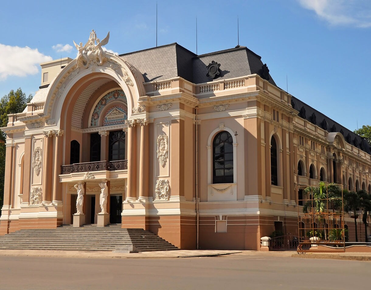 The Saigon Opera House with ornate French colonial architecture, arched windows and statues at the entrance under a bright blue sky.