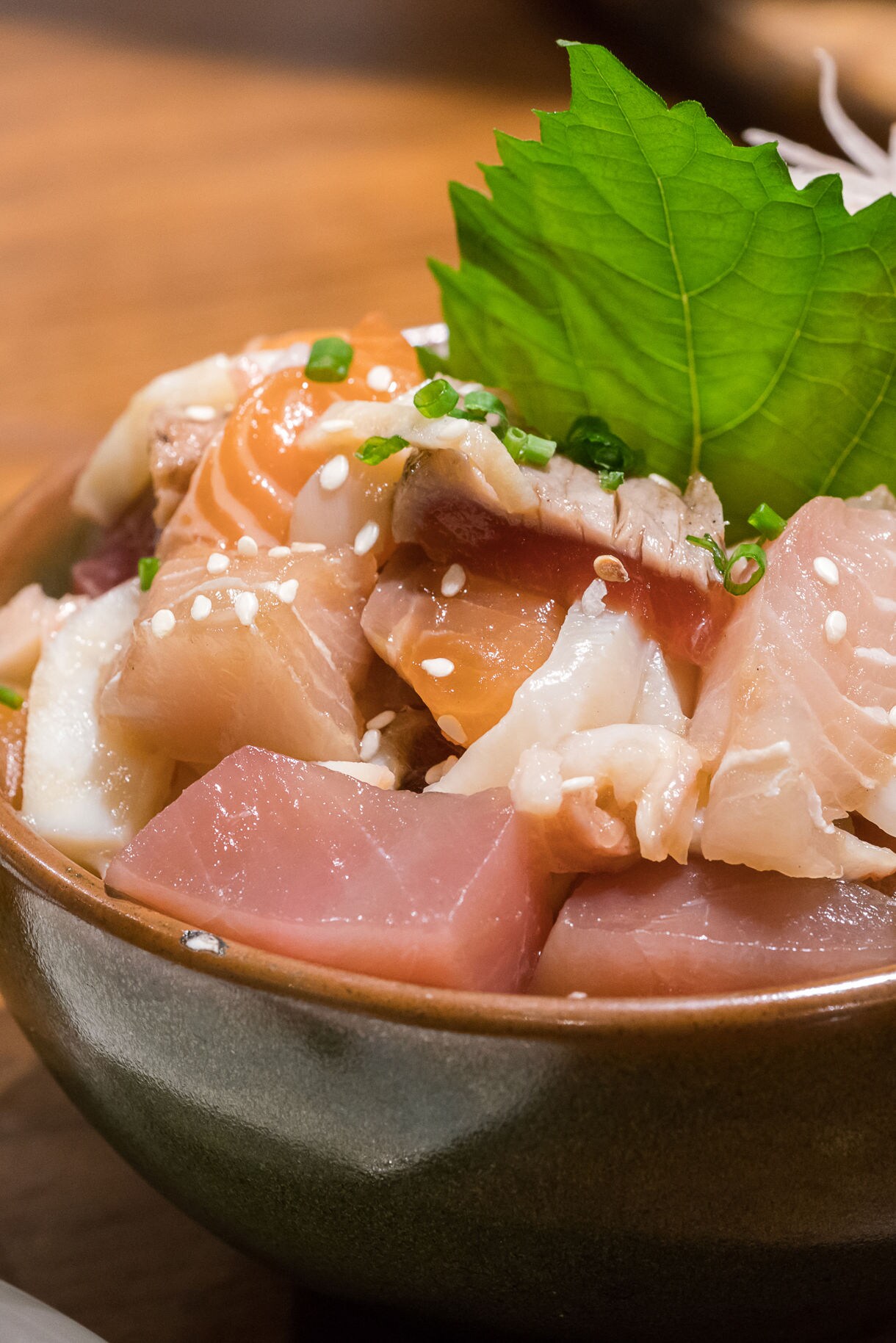 A bowl of fresh sashimi featuring sliced raw fish garnished with green shiso leaves.