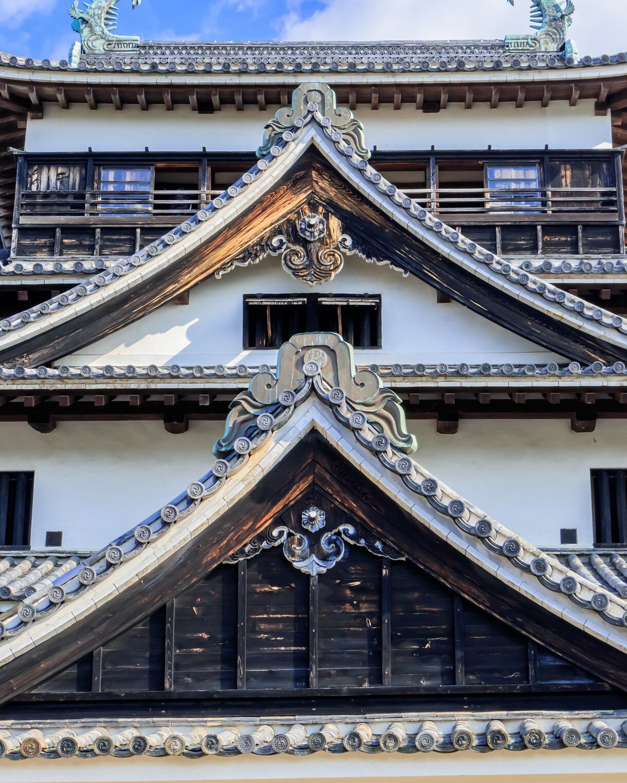 Detailed view of Matsue Castle’s ornate gables and tiled rooftops with phoenix-shaped decorations under a blue sky.