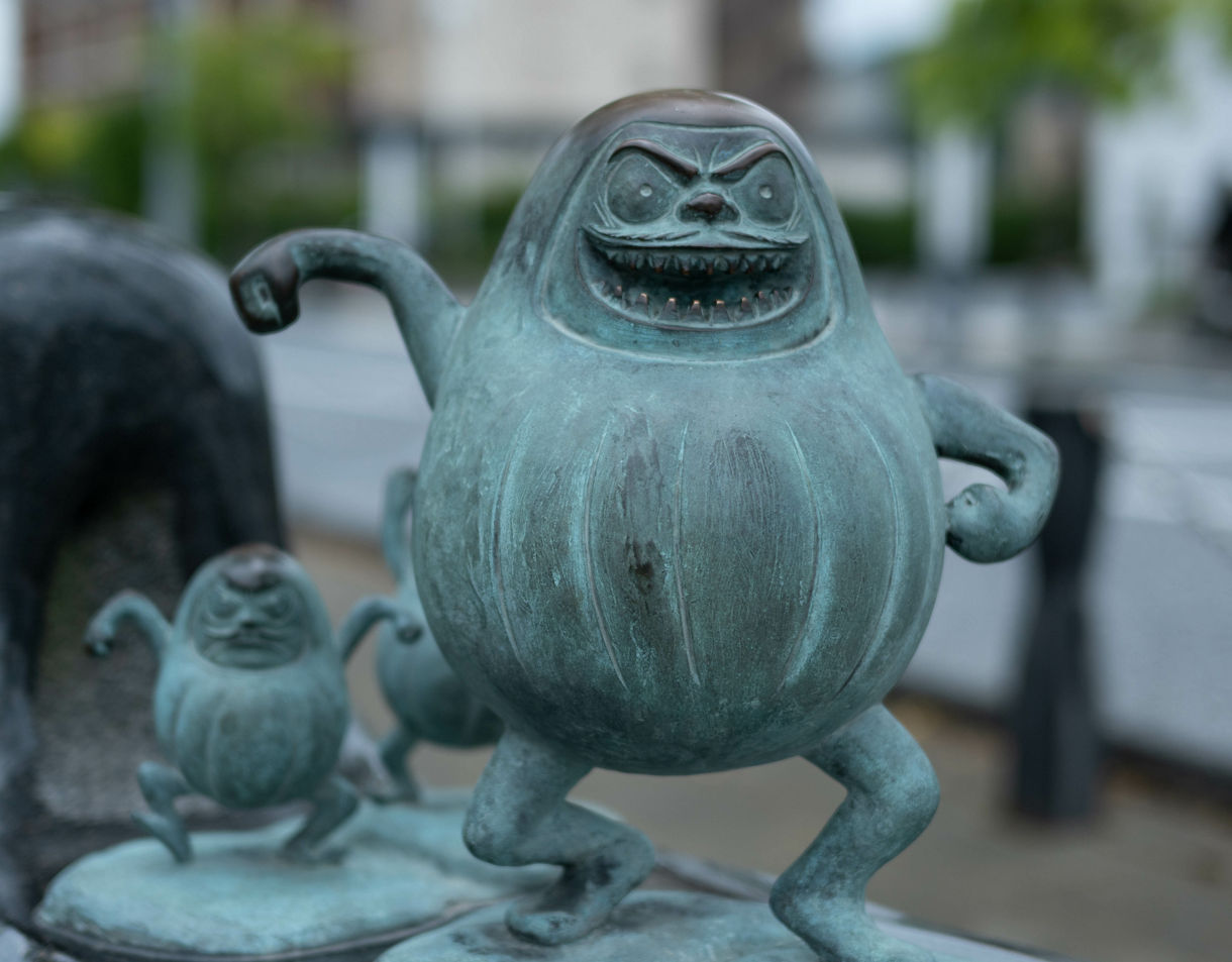 Close-up of playful bronze yokai statue with a toothy grin and round body on Mizuki Shigeru Road in Sakaiminato.