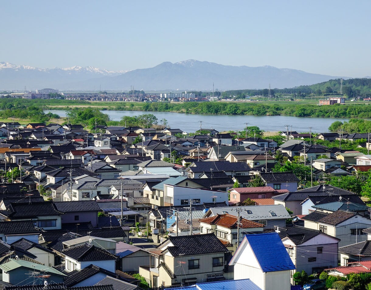 View over Sakata’s traditional homes with a river, green fields and mountains in the background.