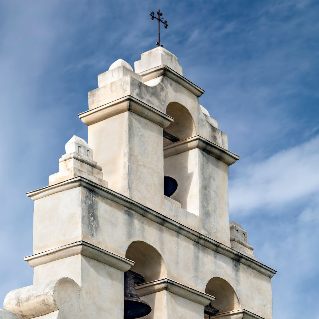 White colonial church bell tower with arched openings and cross on top against blue sky