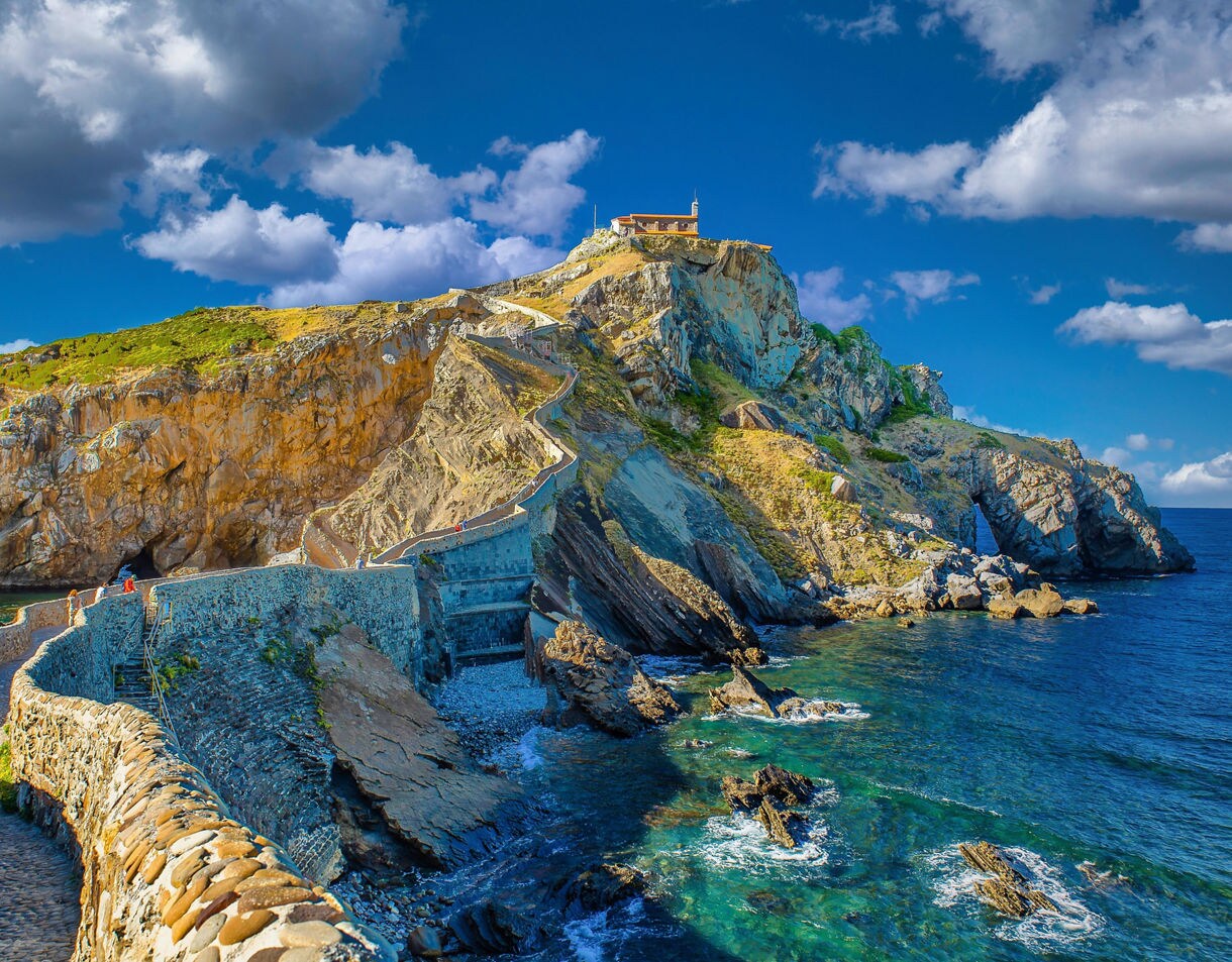 View of the stone bridge and steep stairway leading to San Juan de Gaztelugatxe hermitage perched atop a rocky island on the Basque coast.