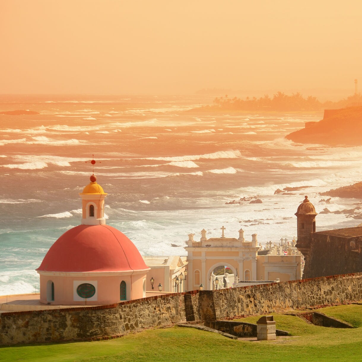 El Morro fortress with distinctive red dome and stone fortifications silhouetted against orange sunset sky over San Juan