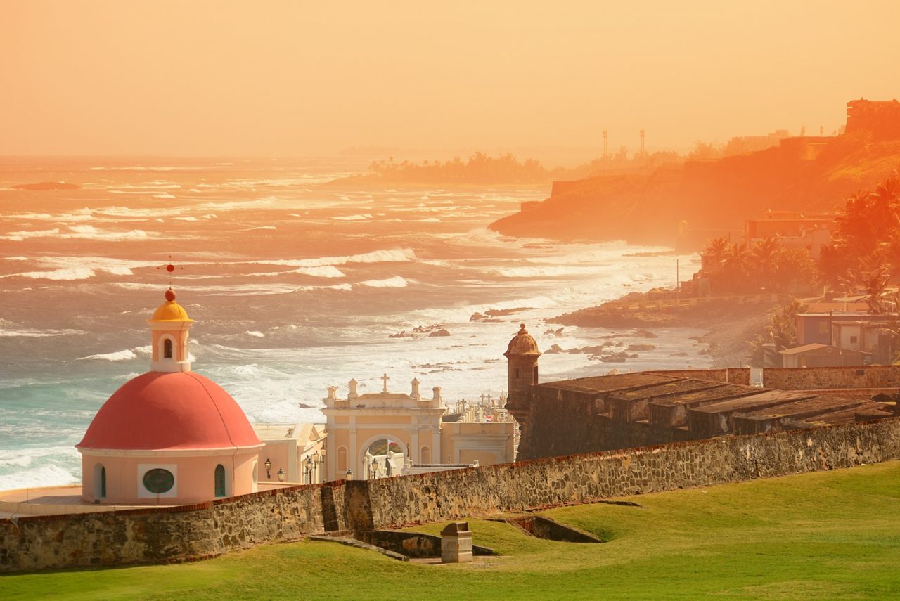 El Morro fortress with distinctive red dome and stone fortifications silhouetted against orange sunset sky over San Juan