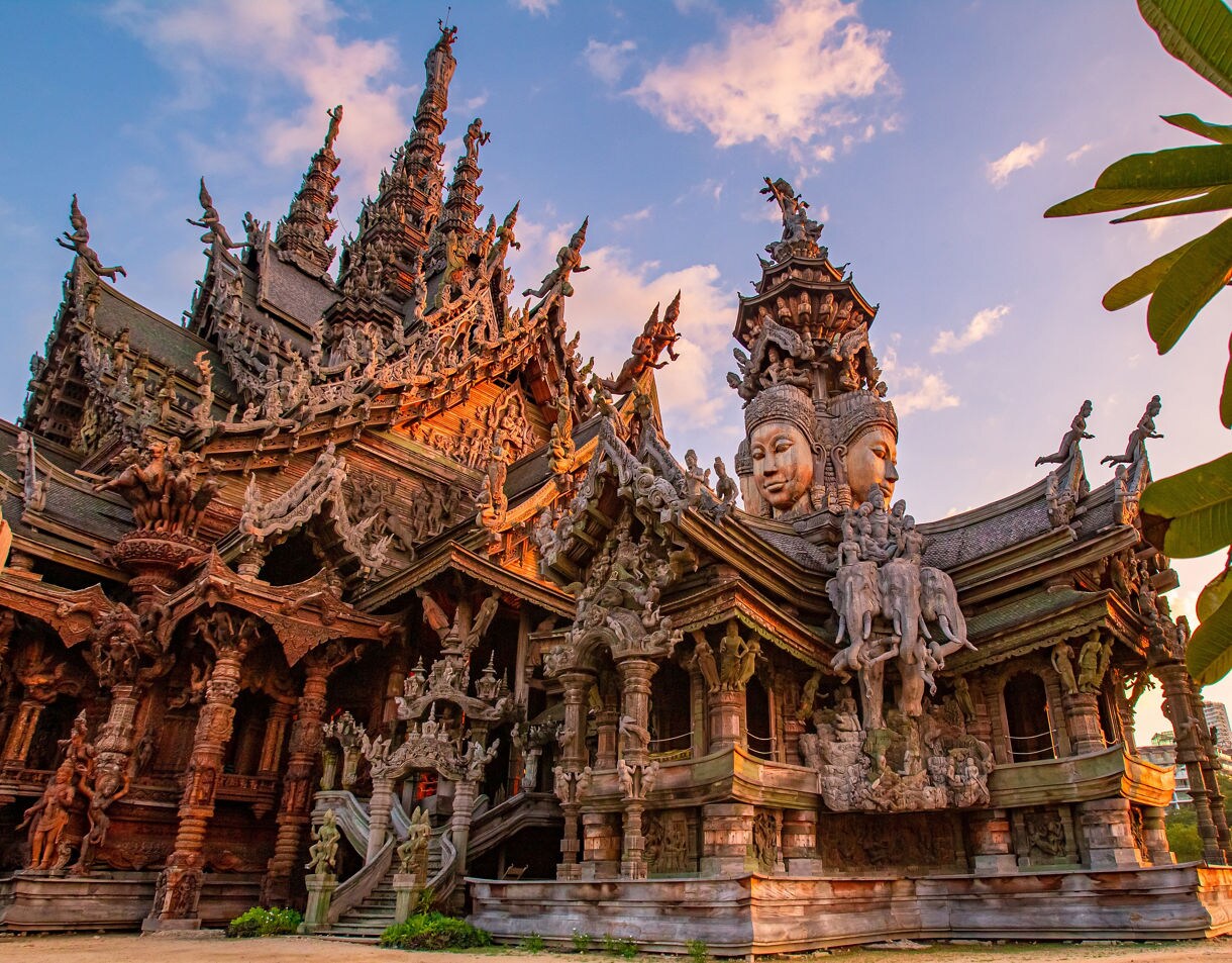 Ornate all-wood temple in Pattaya featuring elaborate carvings of deities, elephants and mythological figures glowing in the sunset light.
